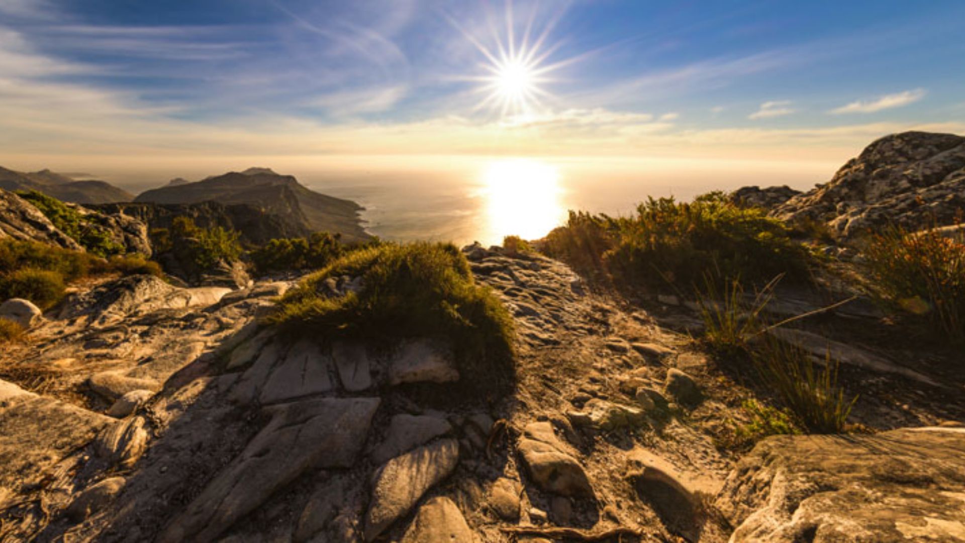 The sun illuminates the ocean and mountains in a serene landscape, highlighting the natural beauty of the scene.