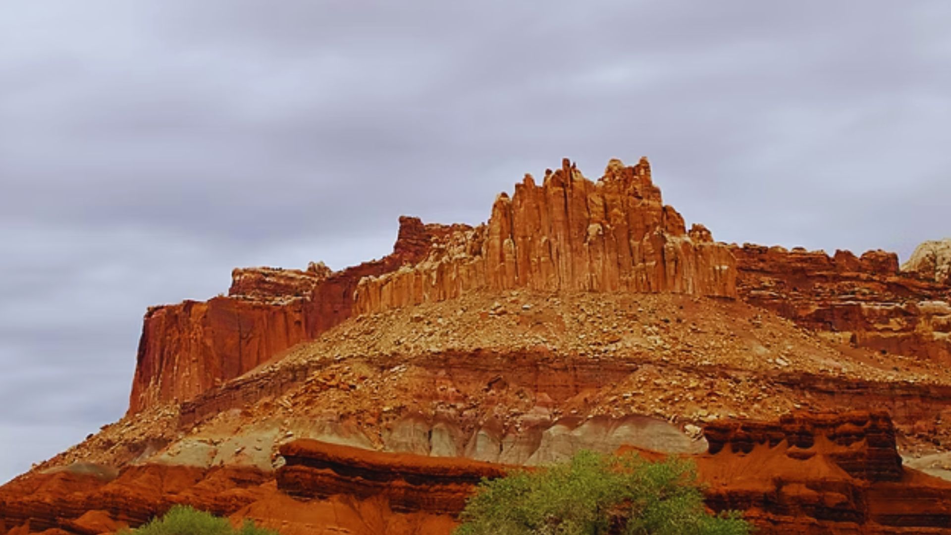 A bold red rock formation dominates the desert landscape, set against a backdrop of wispy clouds.