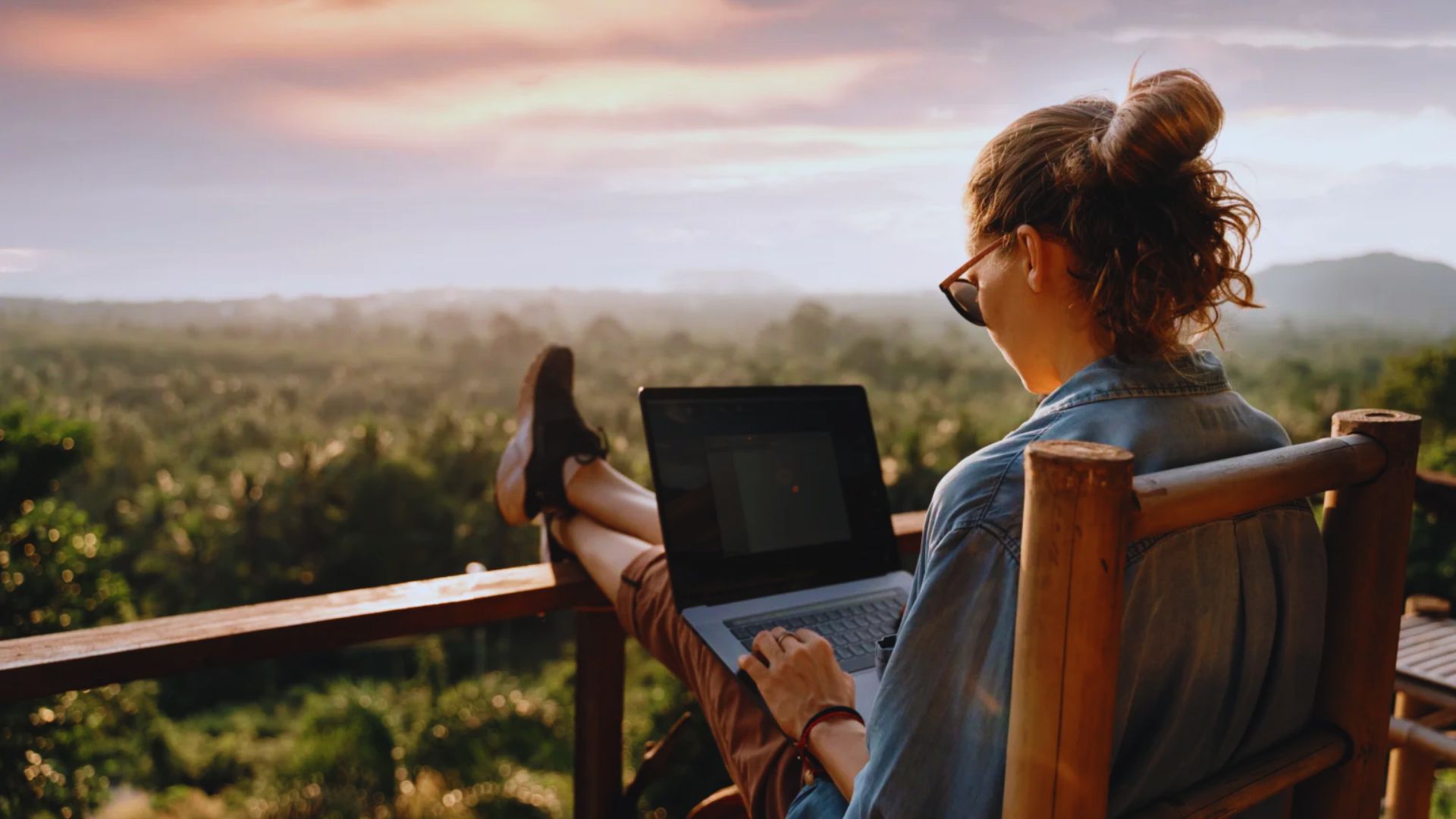 A woman seated on a wooden chair, working on a laptop in a cozy indoor setting.
