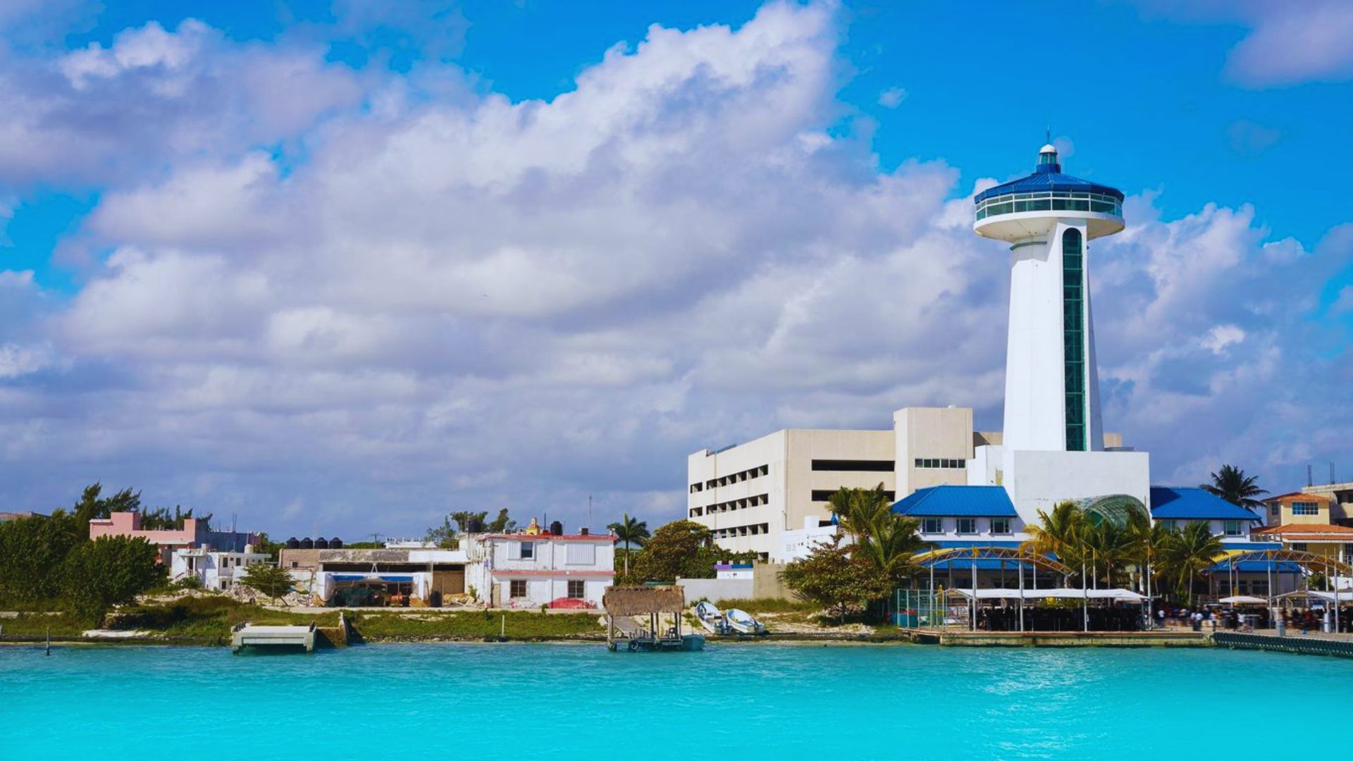A large blue tower with a white roof stands beside calm blue water, creating a serene and picturesque scene.