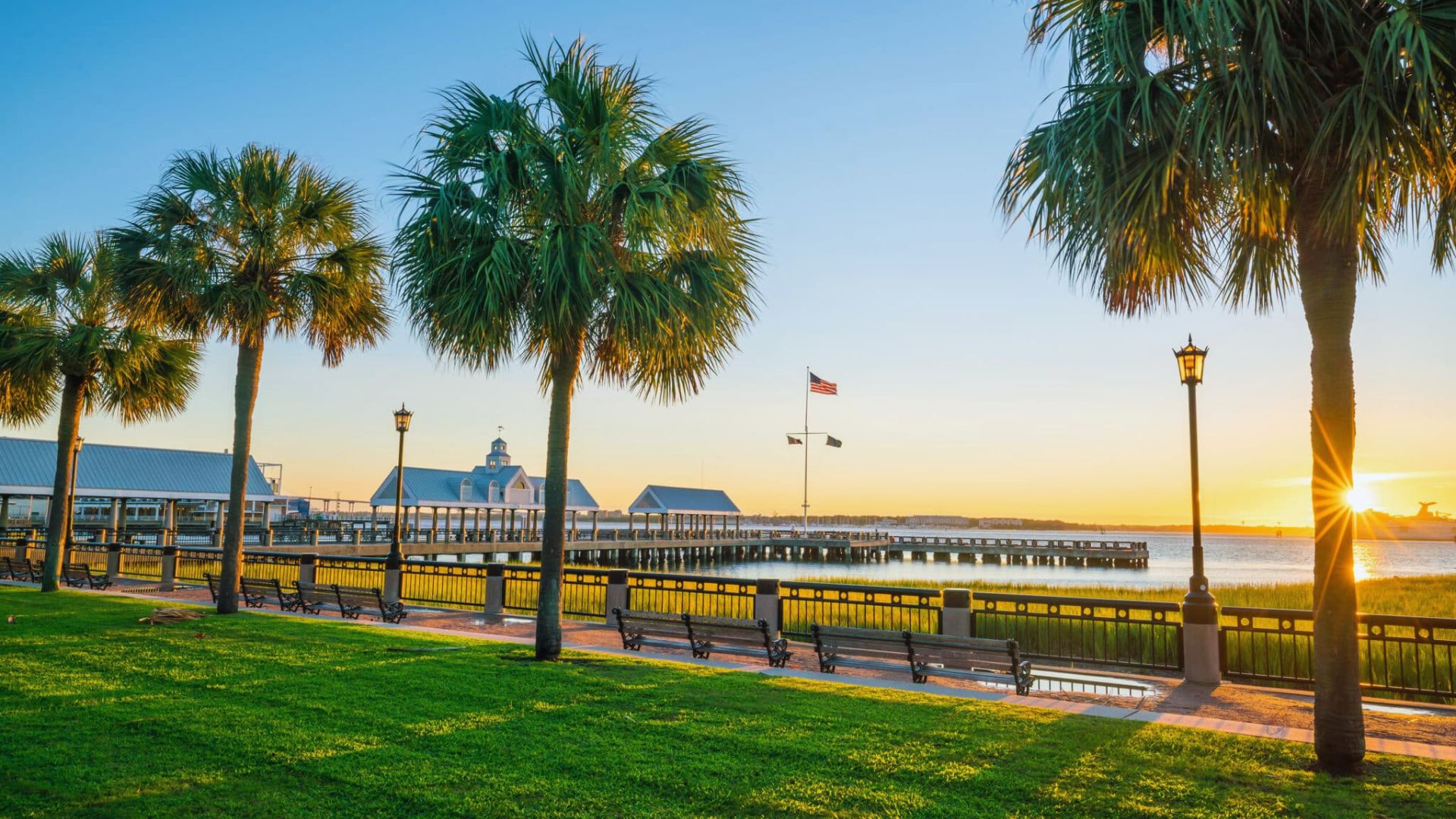 A serene park at sunset featuring palm trees and benches, casting long shadows on the ground.