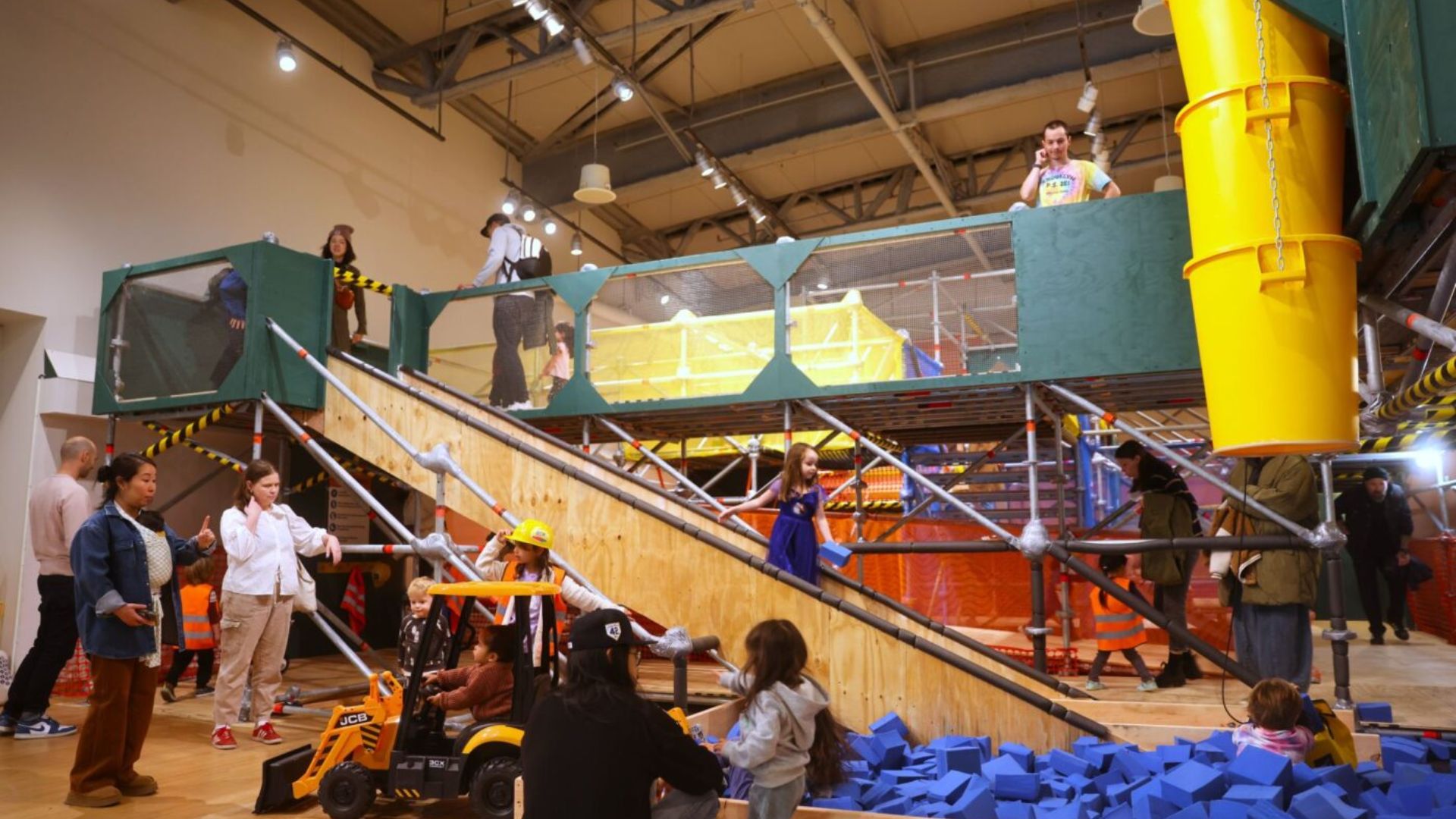 A diverse group of children and adults enjoying activities in a spacious indoor play area filled with colorful structures.
