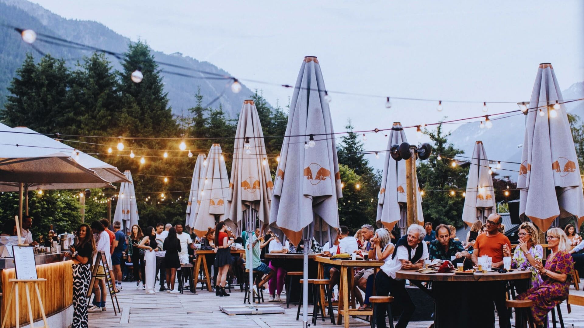Diners seated at tables under umbrellas in a bustling outdoor restaurant setting.
