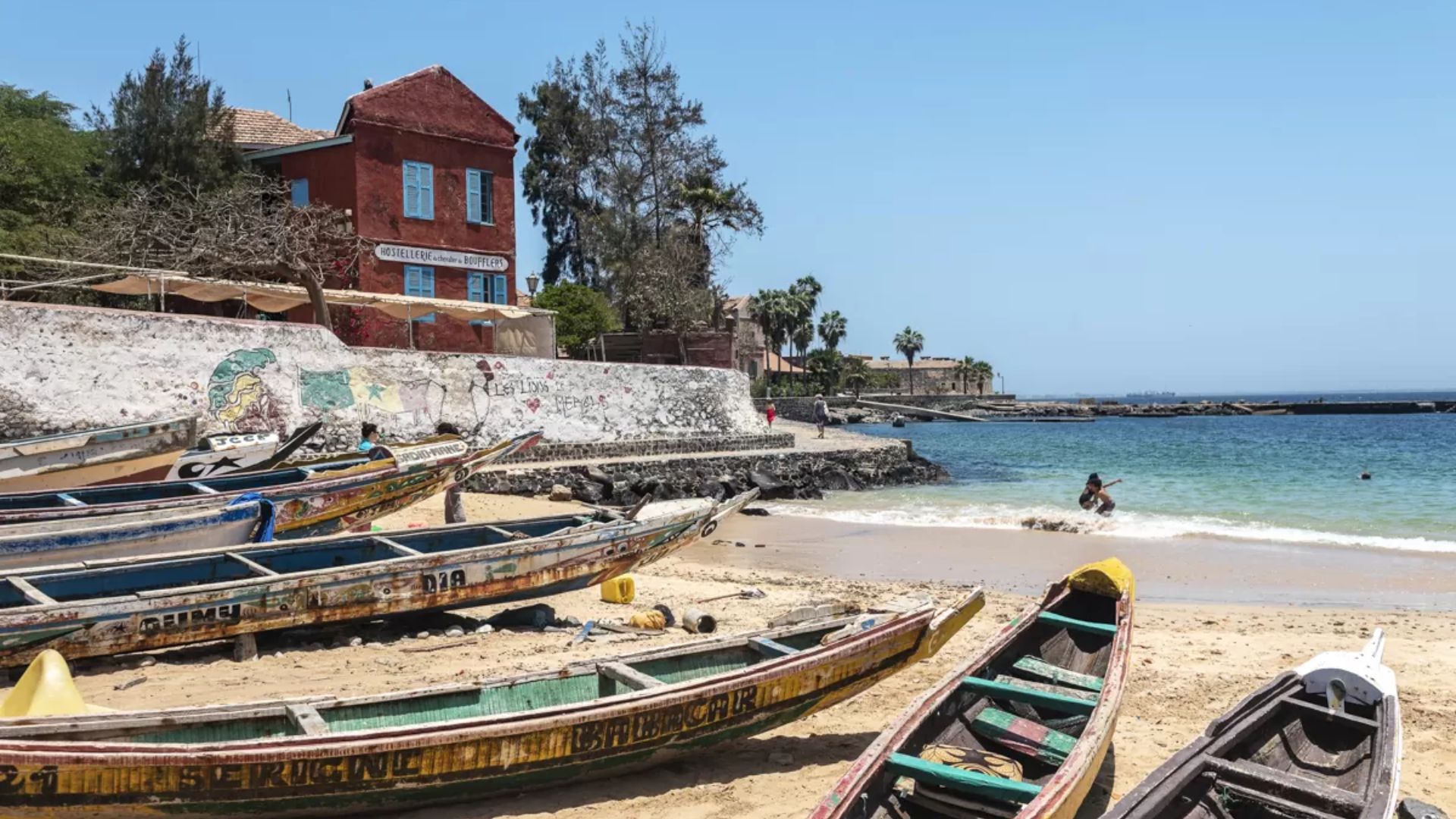 Several boats are lined up along the sandy beach, ready for use under a clear blue sky.