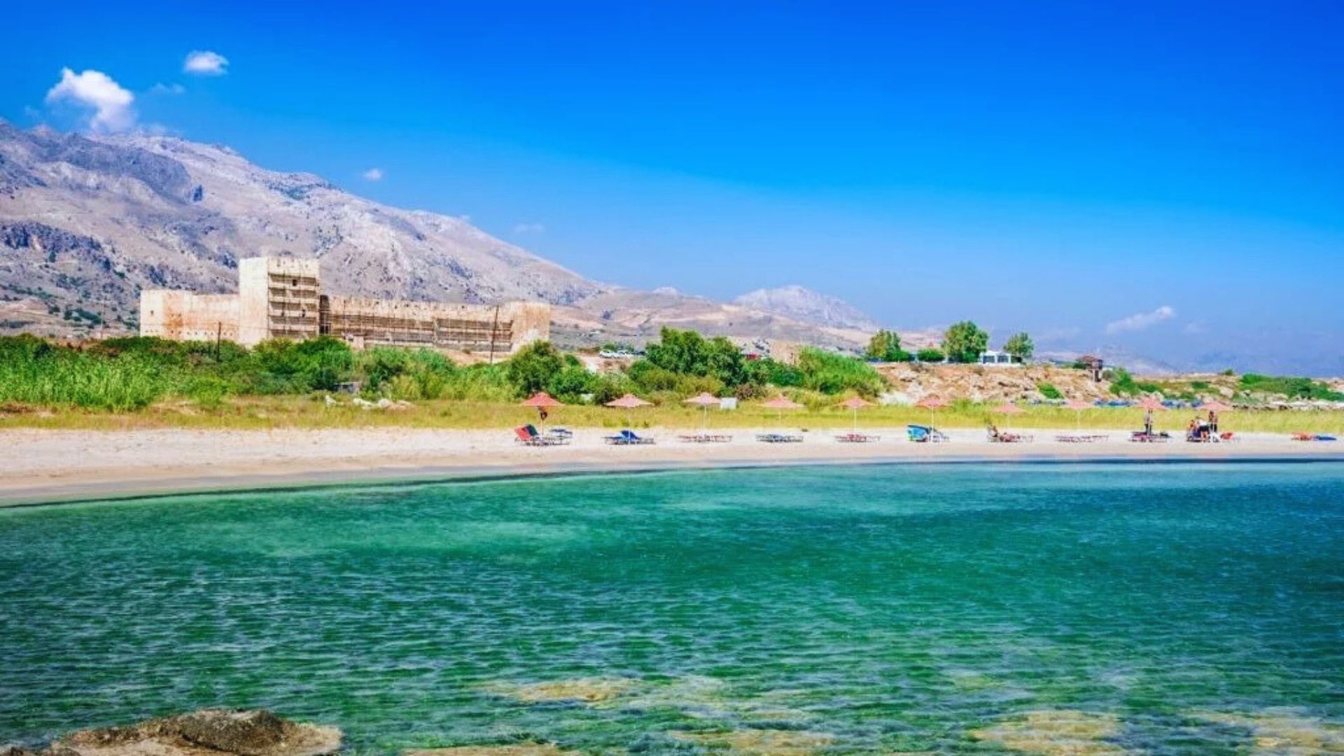 Scenic view of a beach with mountains rising majestically in the background under a clear blue sky.