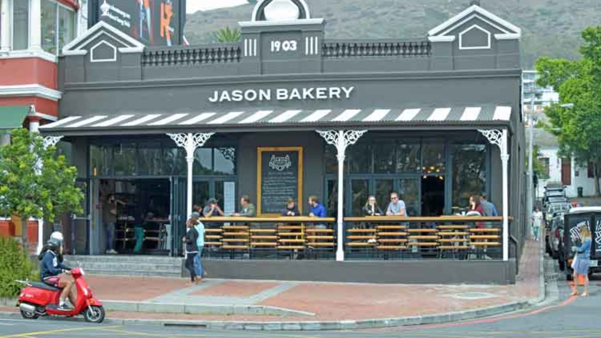 . A bustling restaurant patio with diners enjoying their meals and a motorcycle parked nearby.