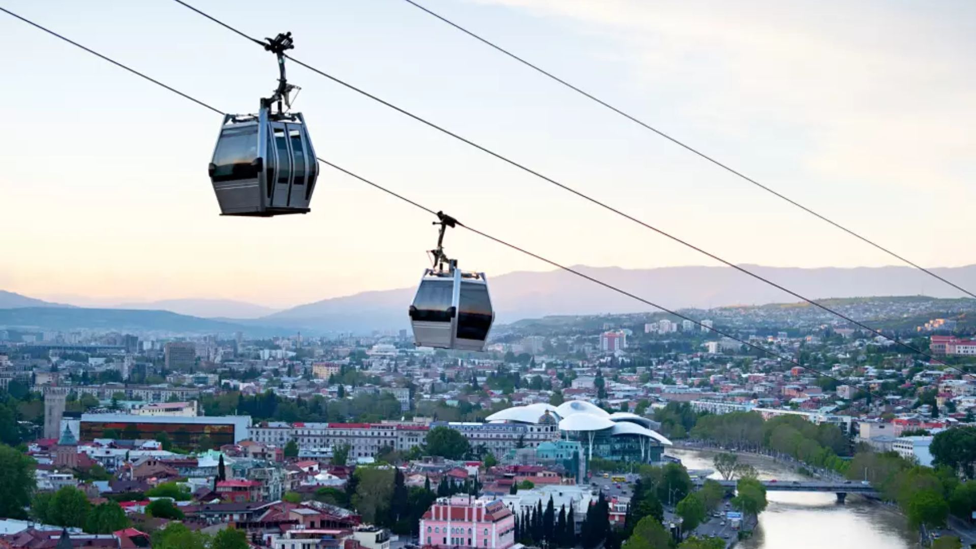 Two cable cars glide above the city skyline, offering a scenic view of the urban landscape below.