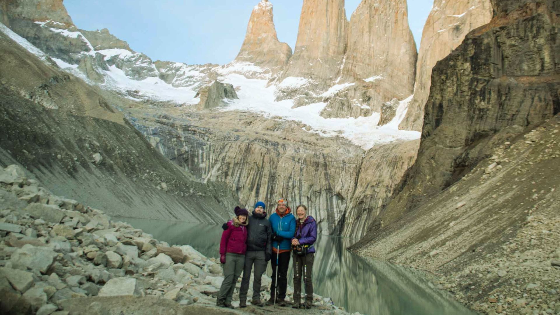 Three people stand on rocky terrain with a mountain backdrop, enjoying the scenic view.
