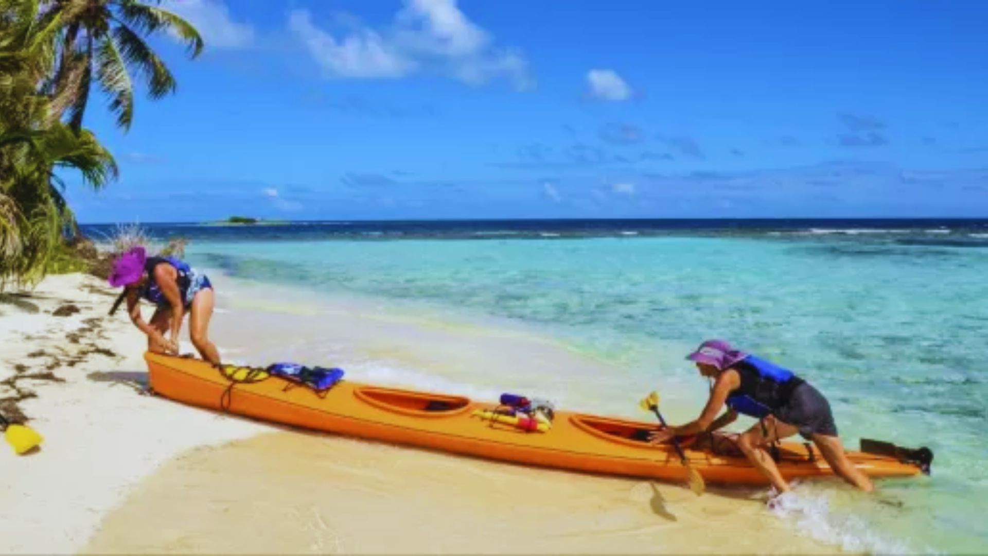 Two individuals loading a kayak onto a beach, preparing for a day of water activities under a clear blue sky.