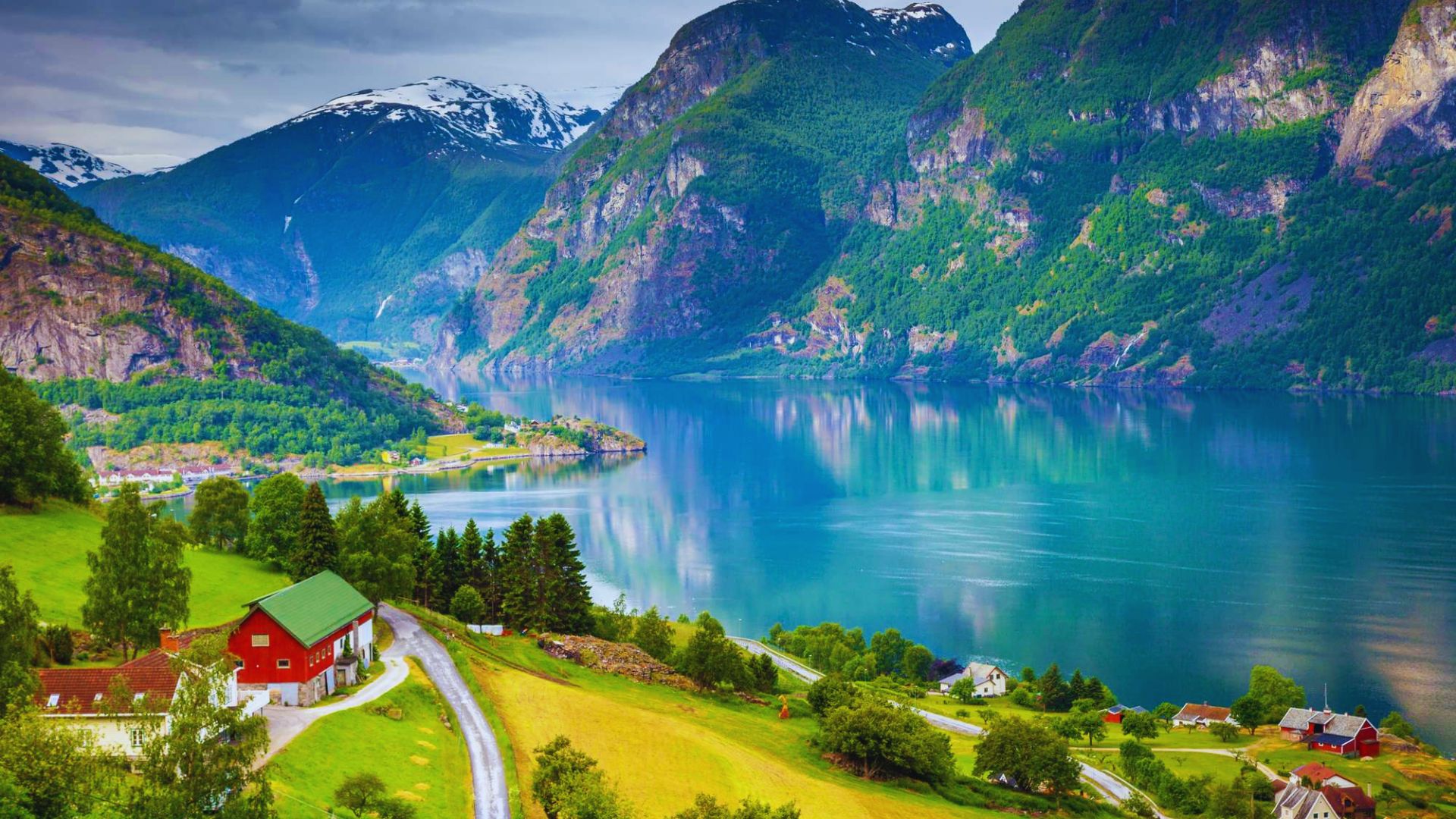 Scenic Norwegian landscape featuring a vibrant red house amidst lush greenery and mountains.