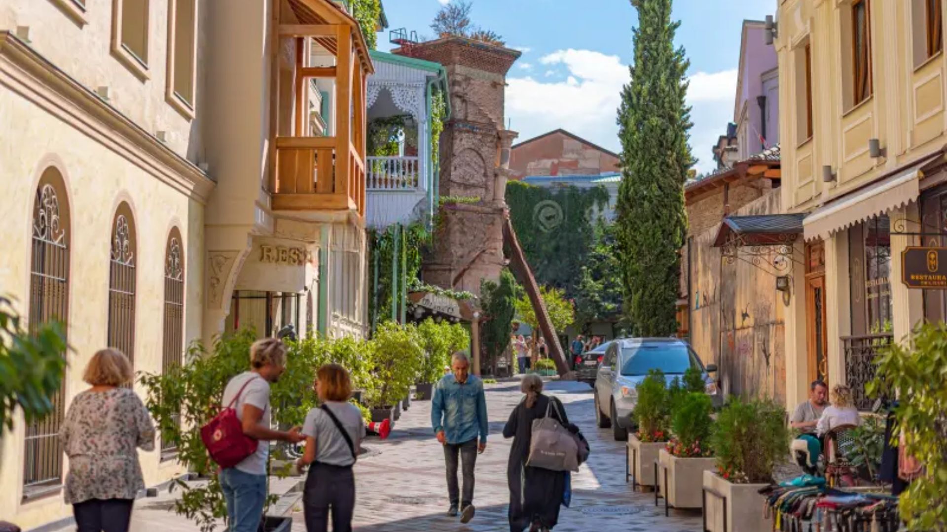 Several pedestrians stroll down a tight urban street, surrounded by city architecture.