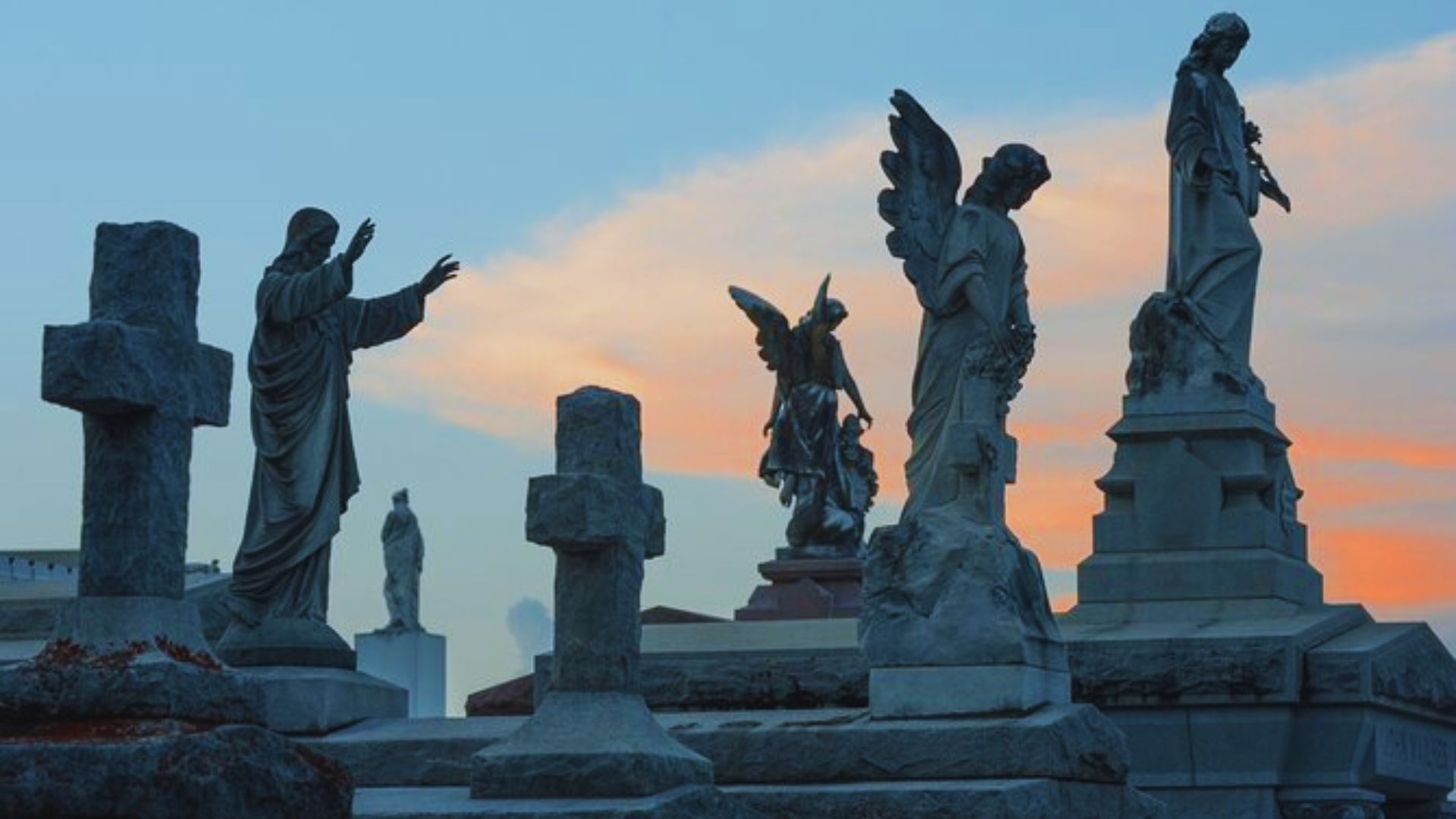 A group of statues silhouetted against a vibrant sunset, casting long shadows on the ground.