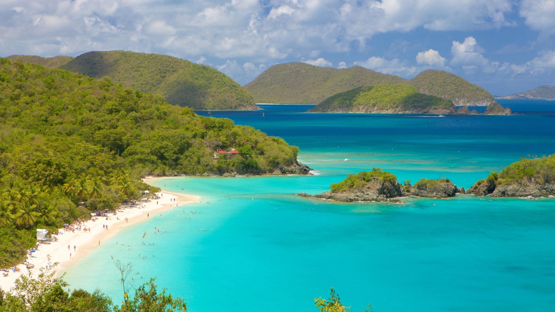 A serene tropical beach with turquoise waters and lush green islands under a blue sky. People stroll along the white sandy shore, evoking a peaceful vibe.