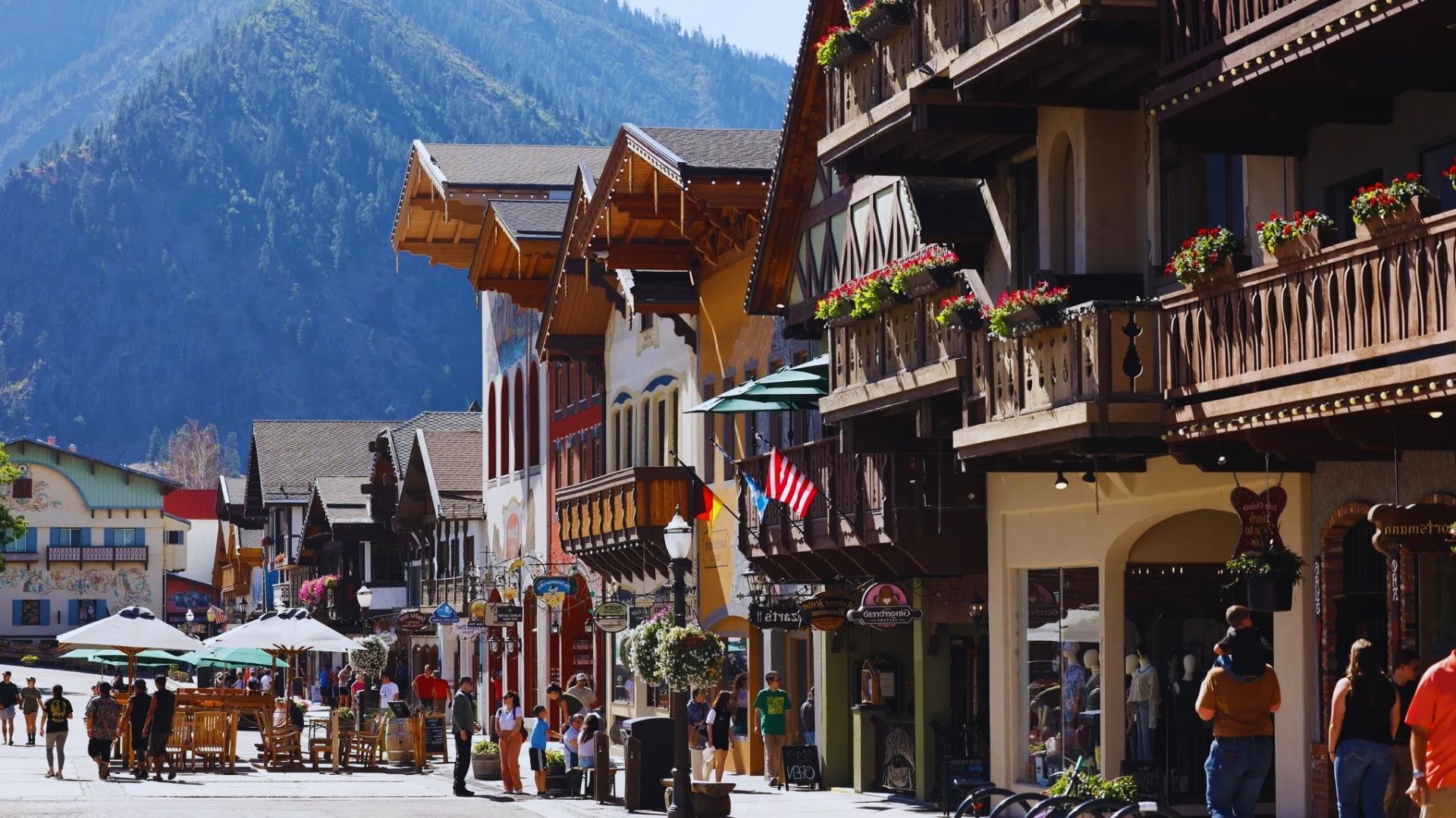 A bustling street scene with people shopping and walking, set against a backdrop of majestic mountains.