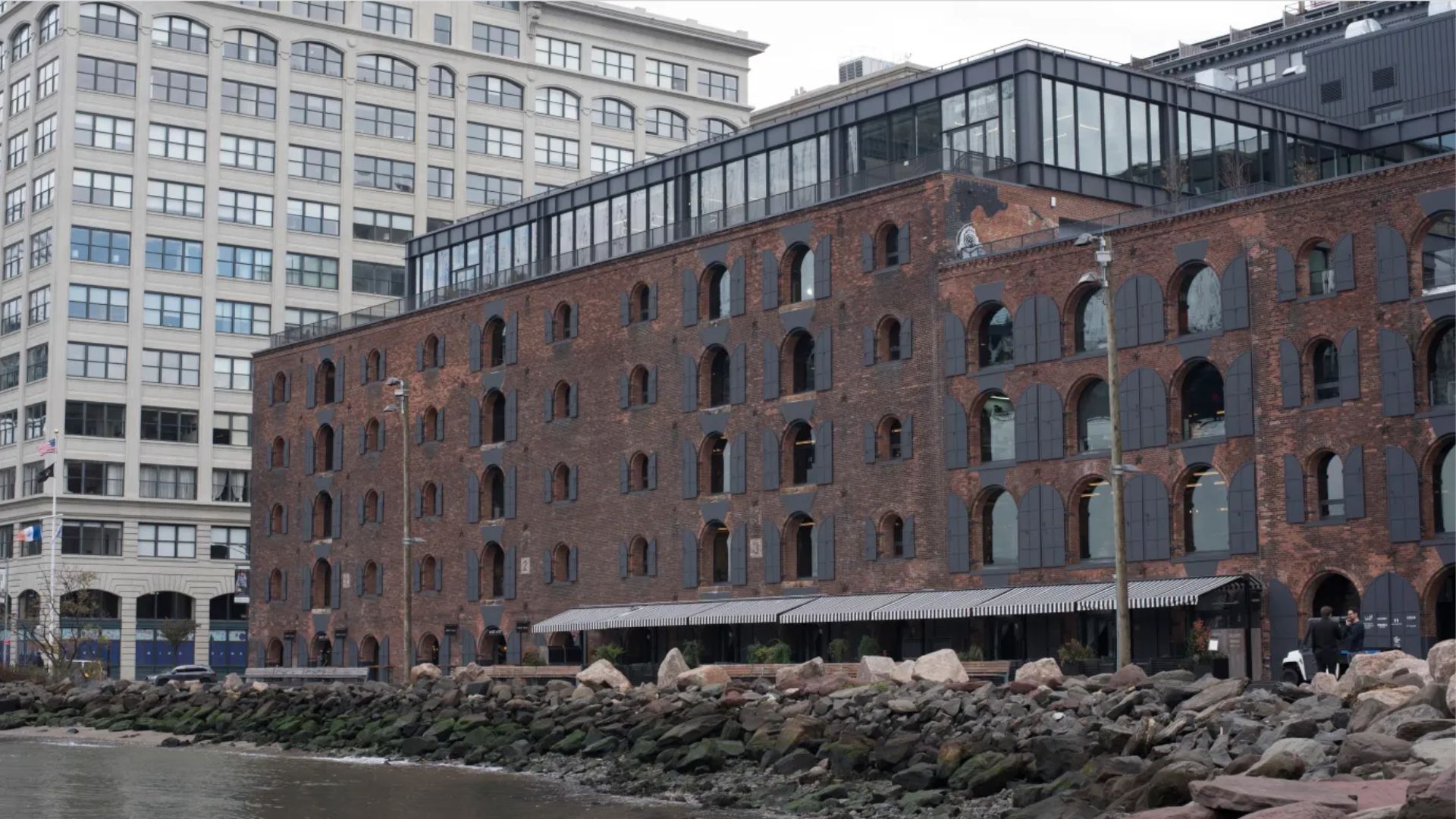 An old brick building stands beside a calm body of water, reflecting its historic architecture.
