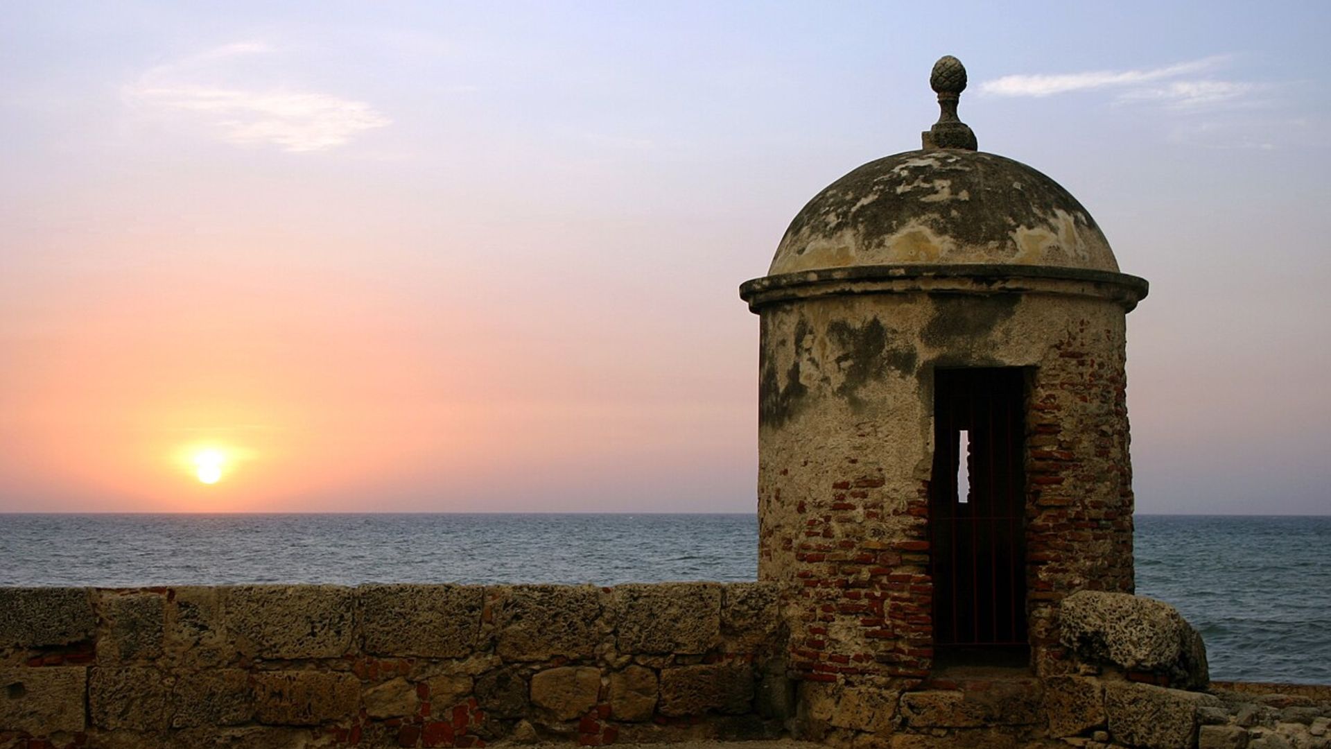 A tower stands tall at sunset, framed by a serene ocean view in the background.