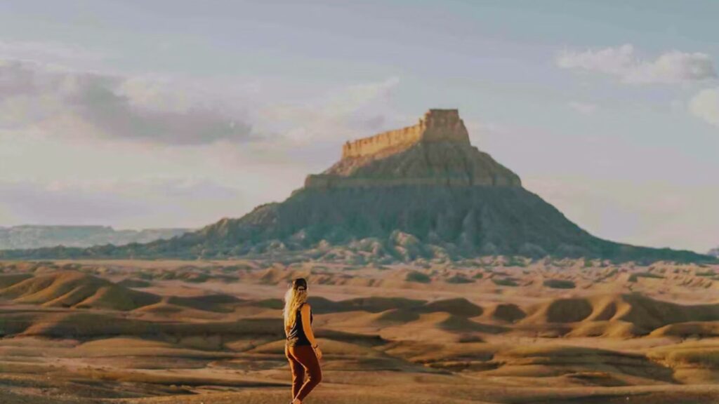A woman stands in a vast desert, with a mountain range rising majestically in the background.