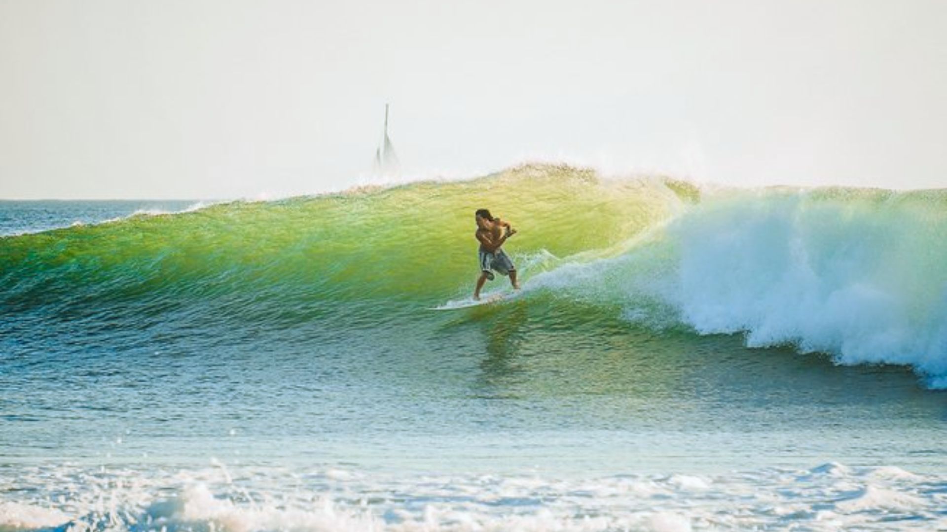 Surfer riding a large, translucent green wave, sun glistening on the water. A sense of freedom and exhilaration in an open ocean setting.