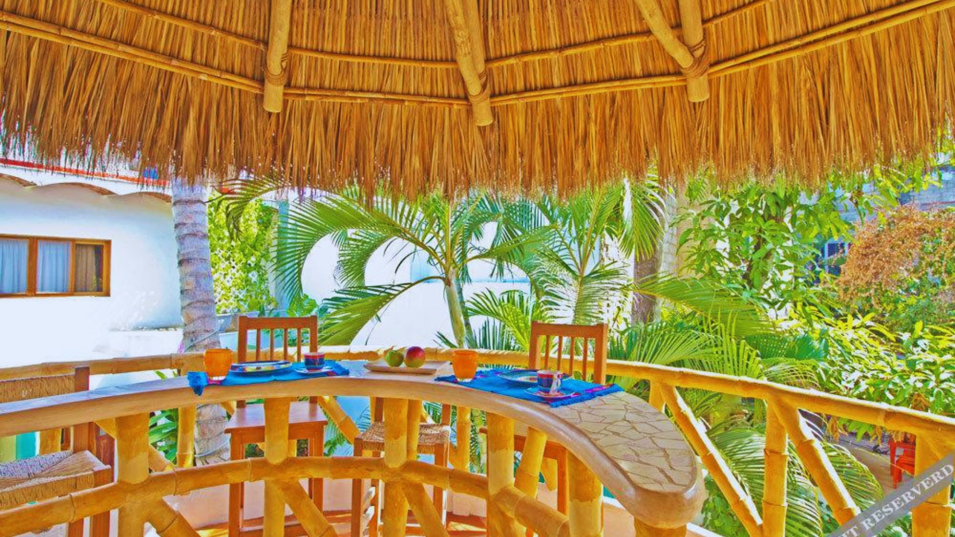 A tropical outdoor dining area with palm trees and lush greenery, featuring a curved wooden bar with stools under a thatched roof, exuding a serene and inviting ambiance.