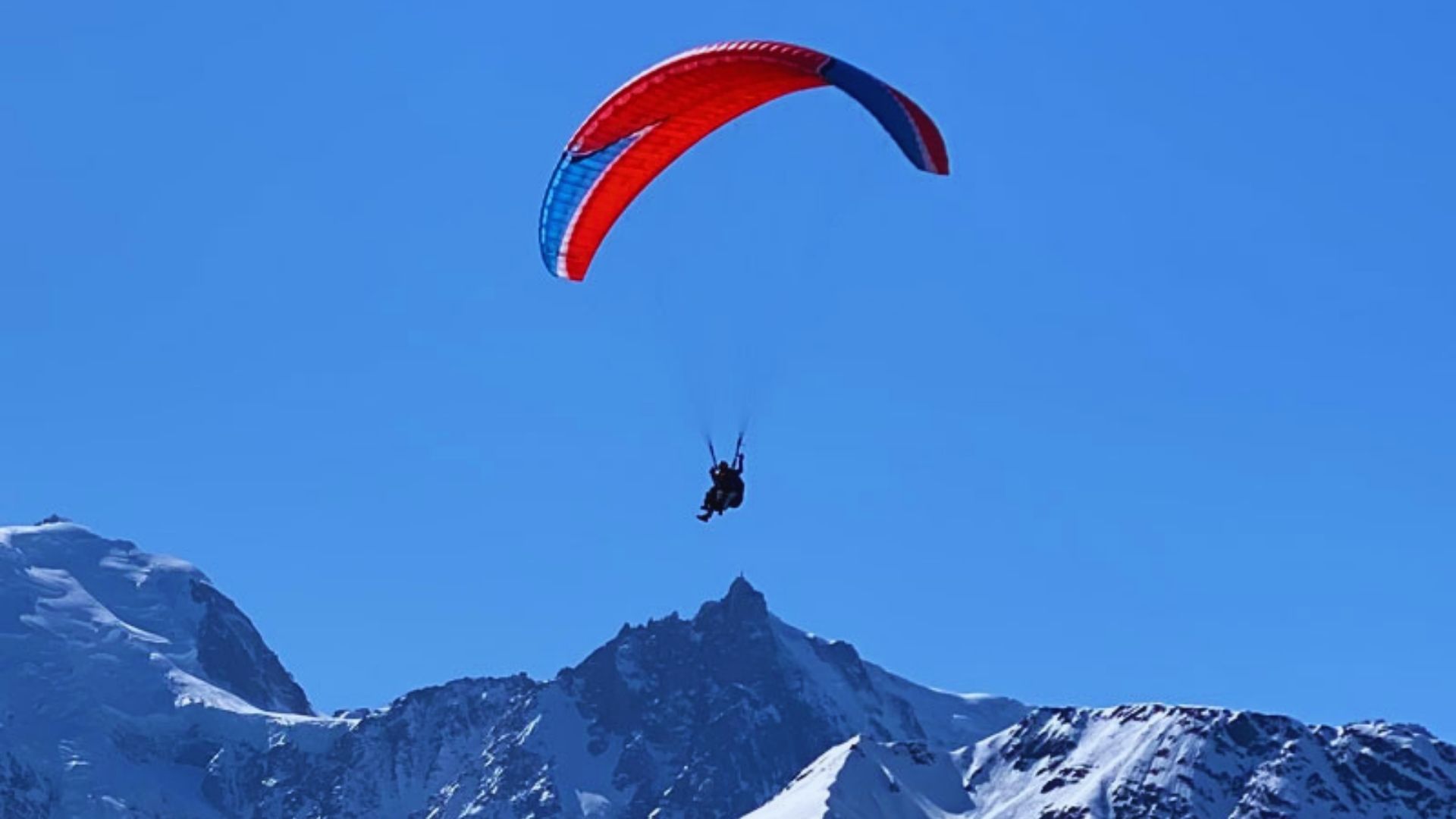 A person paragliding gracefully above a stunning mountain range under a clear blue sky.
