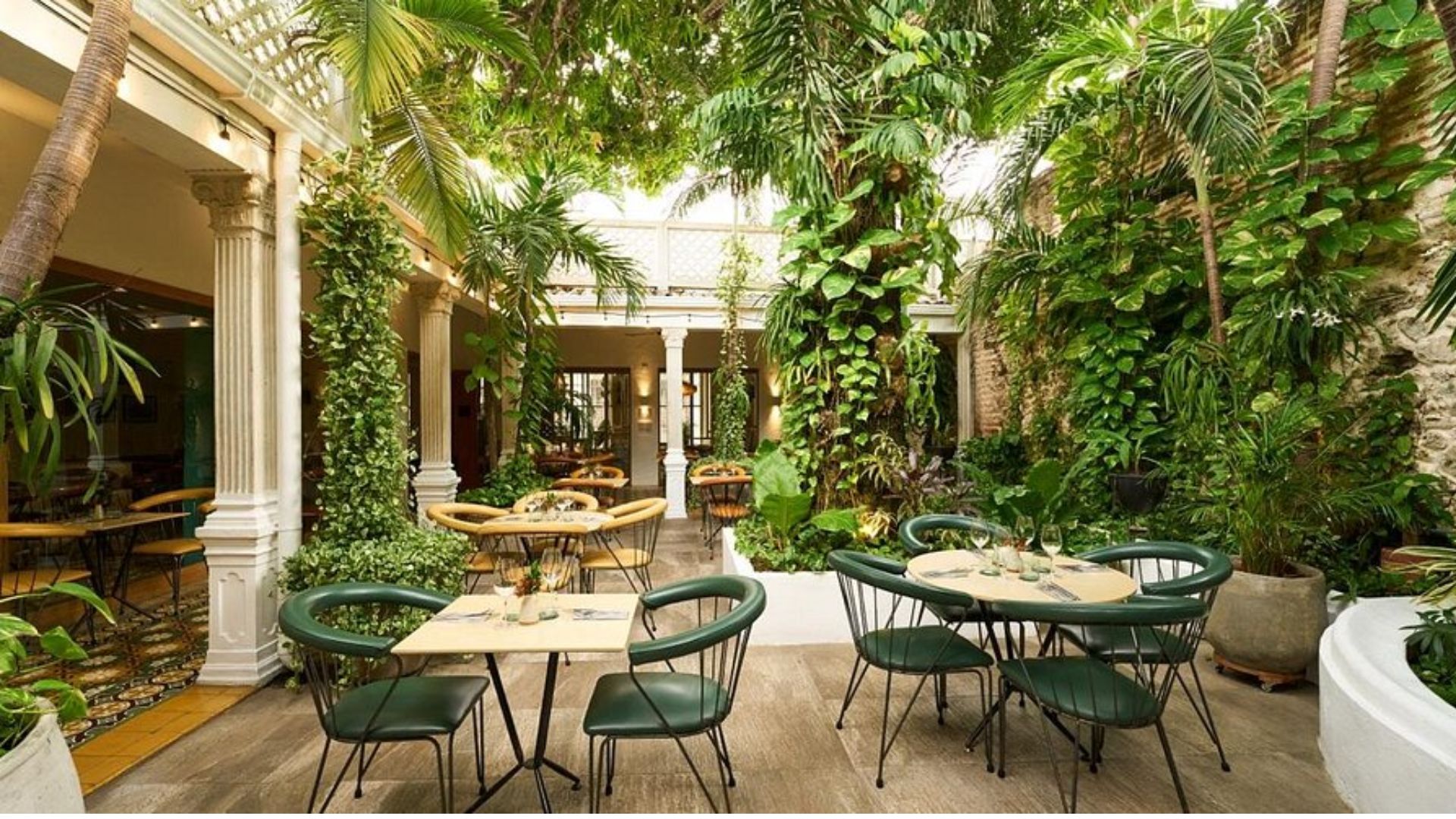A restaurant set in a garden, featuring tables and chairs arranged among lush greenery.
