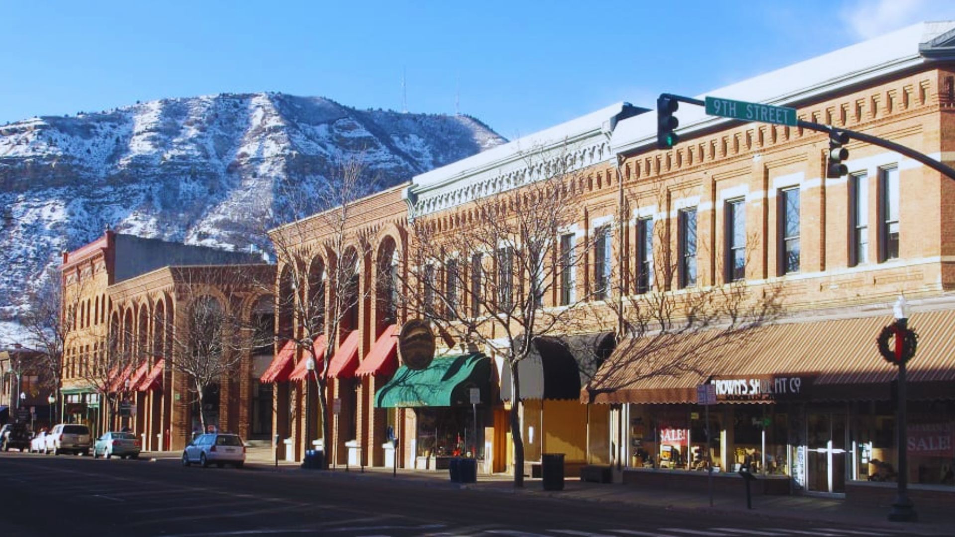 A bustling city street lined with shops, with a majestic mountain rising in the background.