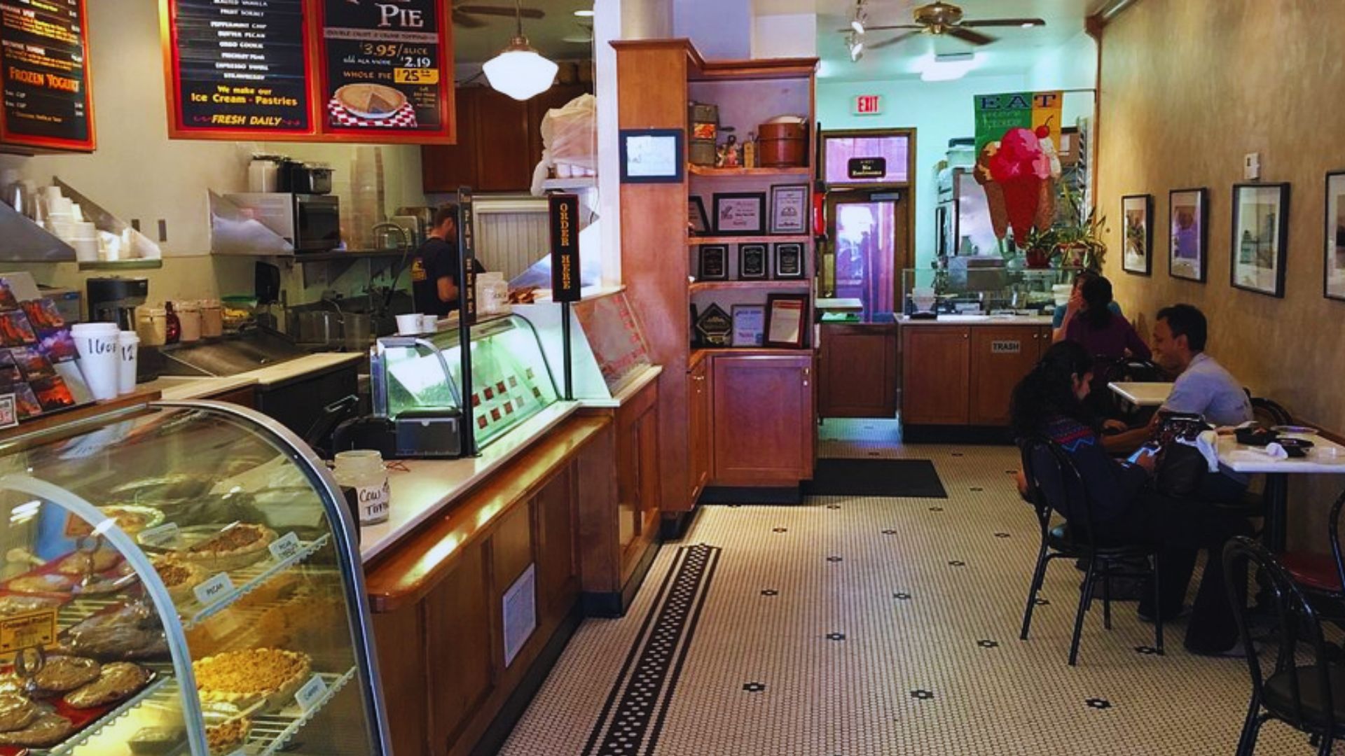 Inside a bakery, customers are seated at tables, savoring food and drinks in a lively, cozy environment.