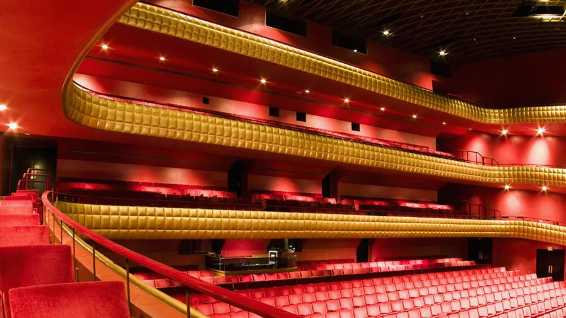 A luxurious theater interior featuring red velvet seats, gold-accented balconies, and soft lighting, creating an ambiance of elegance and anticipation.
