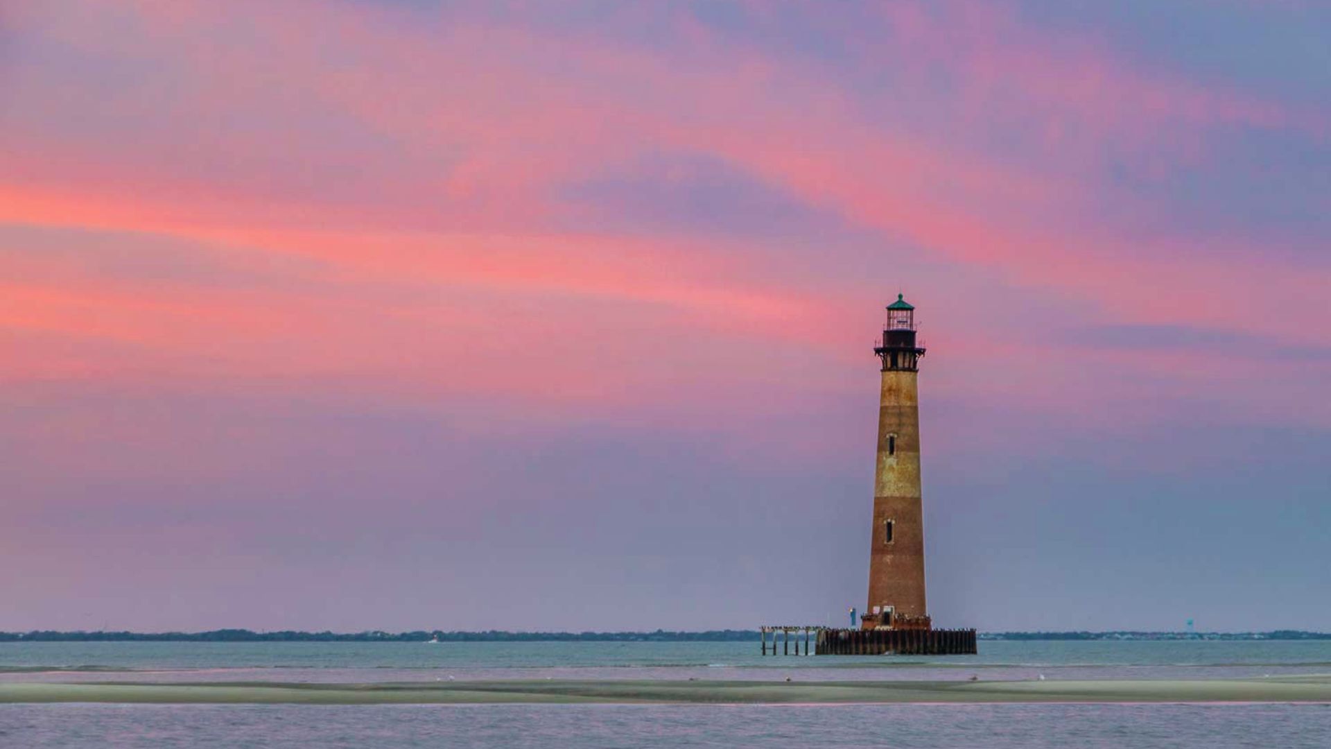 Lighthouse silhouette against a vibrant sunset sky, captured by Jimmy Kirk.