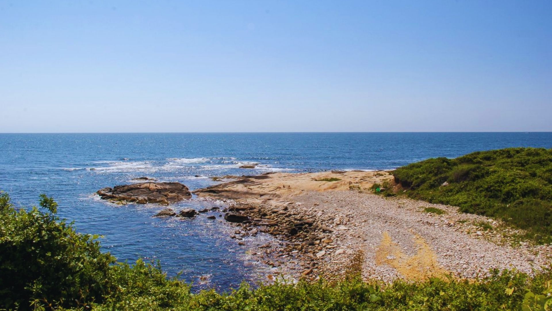 A scenic view of the ocean from a rugged rocky shore, with waves gently crashing against the rocks.