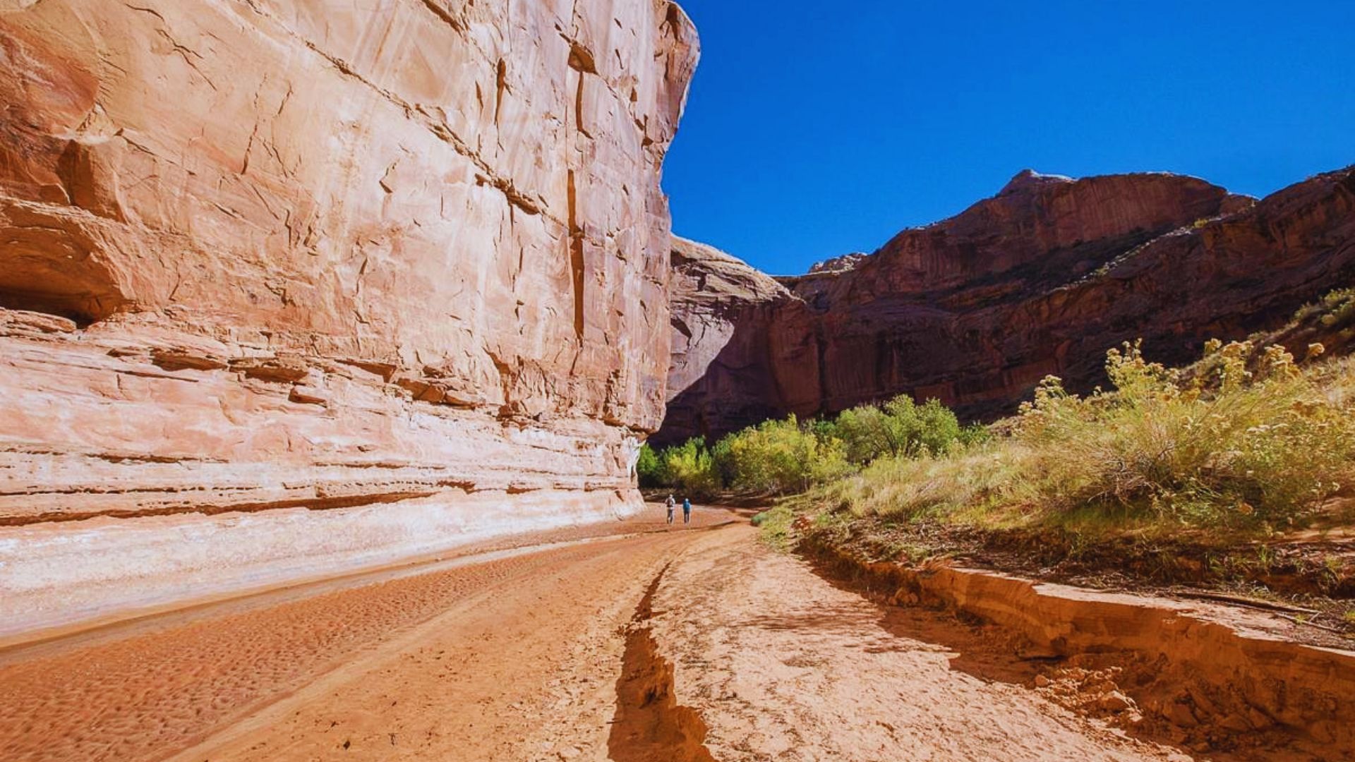 A person walks along a dirt road through a scenic canyon, surrounded by towering rock formations.