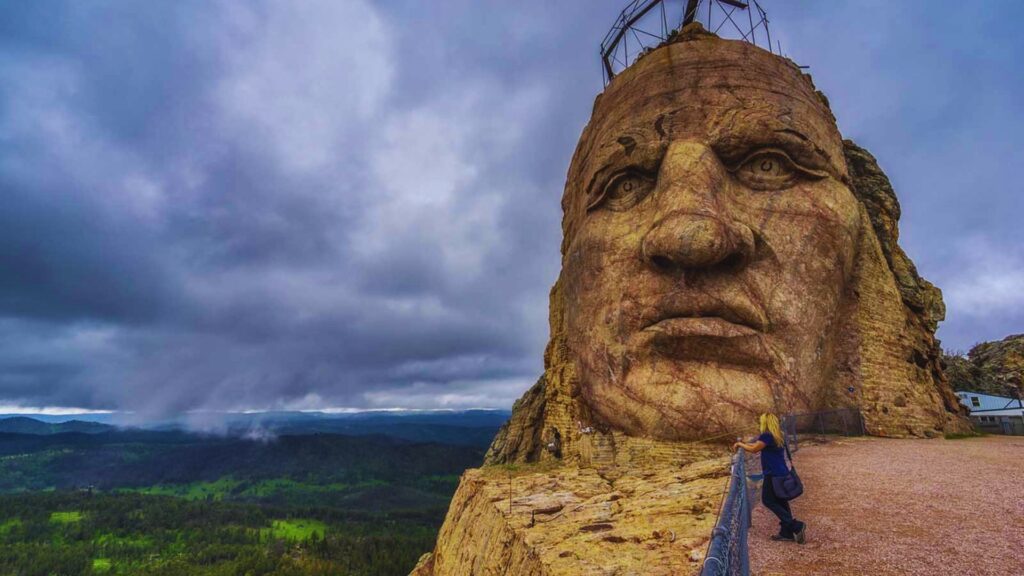 A massive mountain face features a detailed sculpture carved into its rock surface.