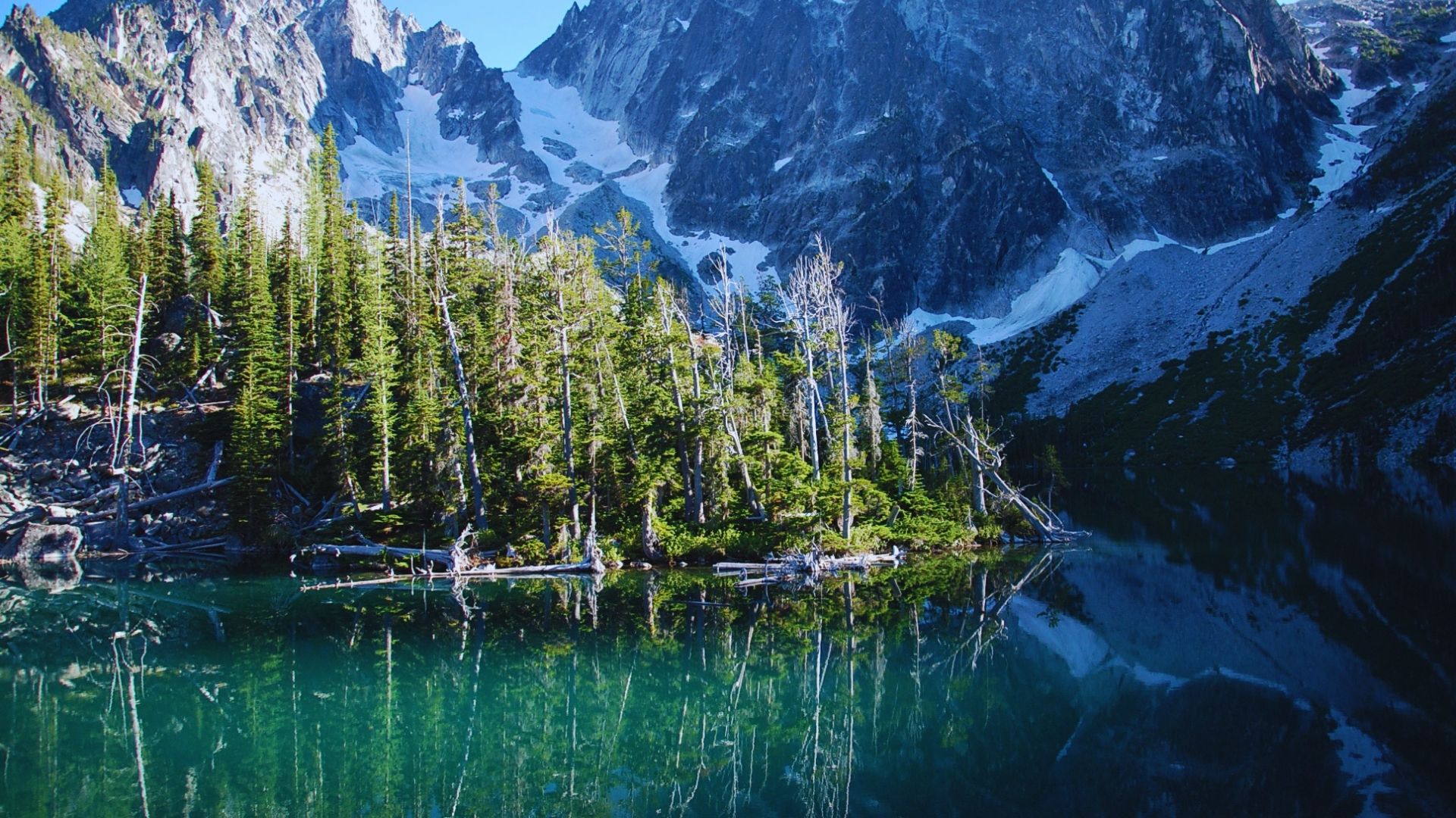 A serene mountain range is mirrored in the calm surface of a lake, creating a picturesque natural scene.