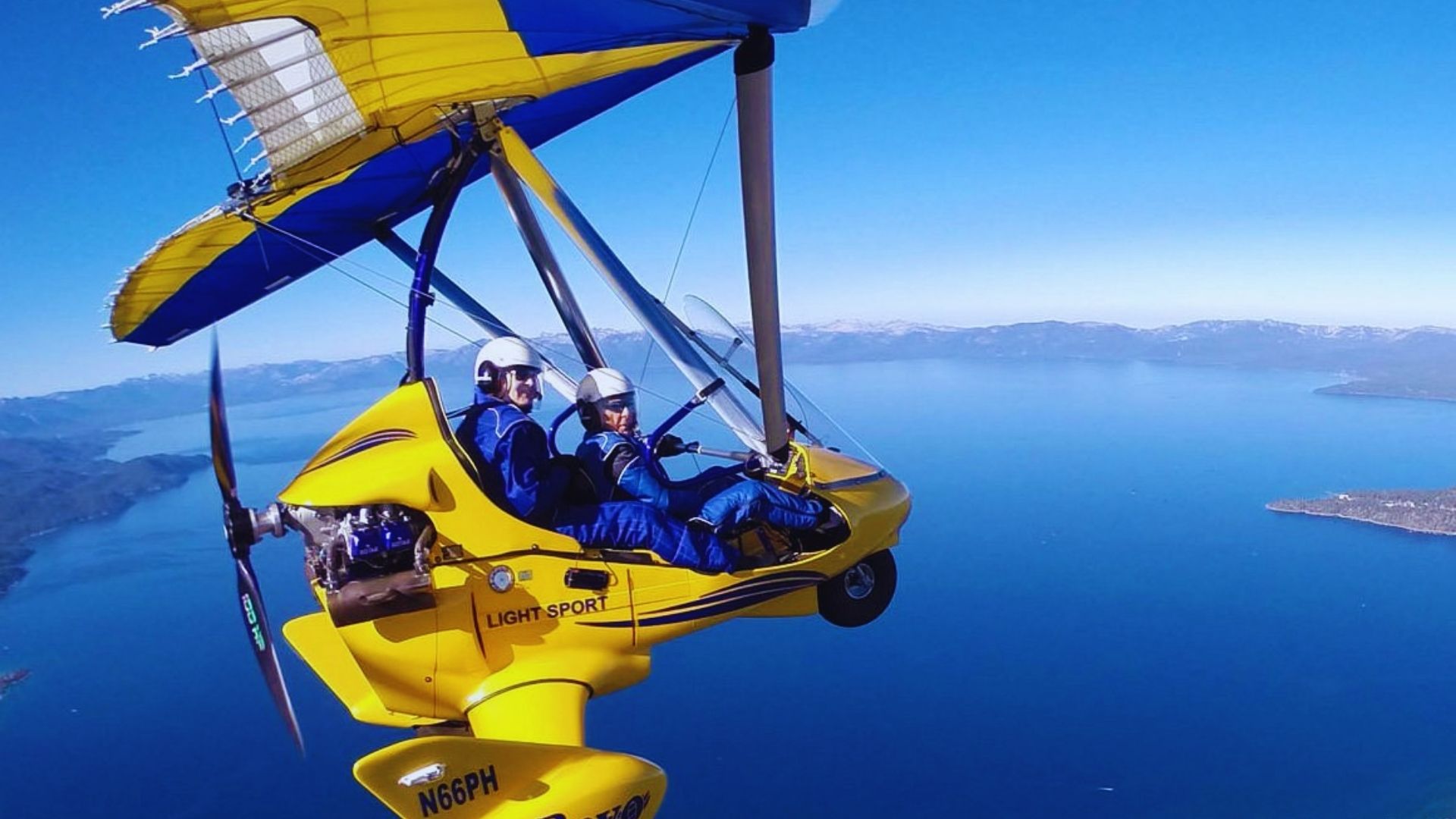 Two individuals soaring in a yellow and blue hang glider against a clear sky.