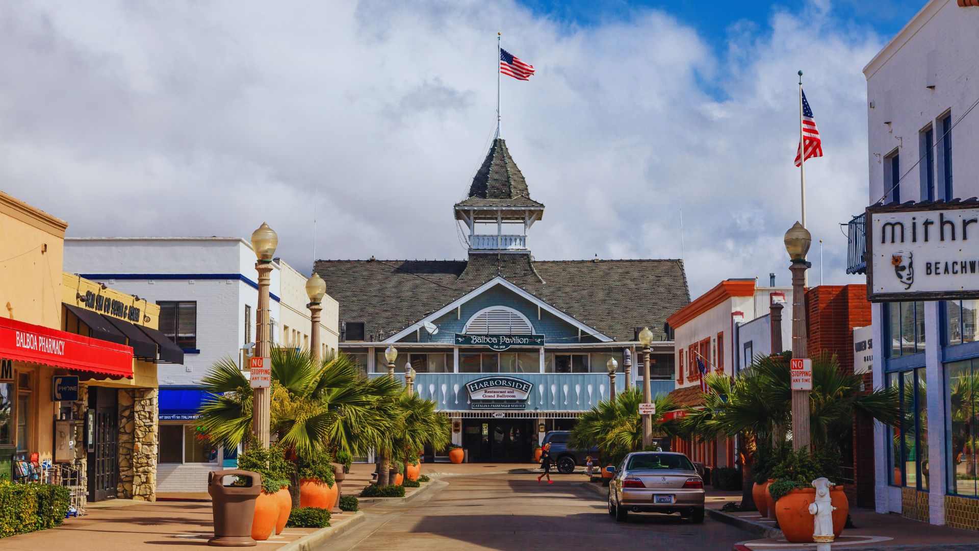 A vibrant street lined with shops, featuring palm trees swaying in the background under a clear blue sky.