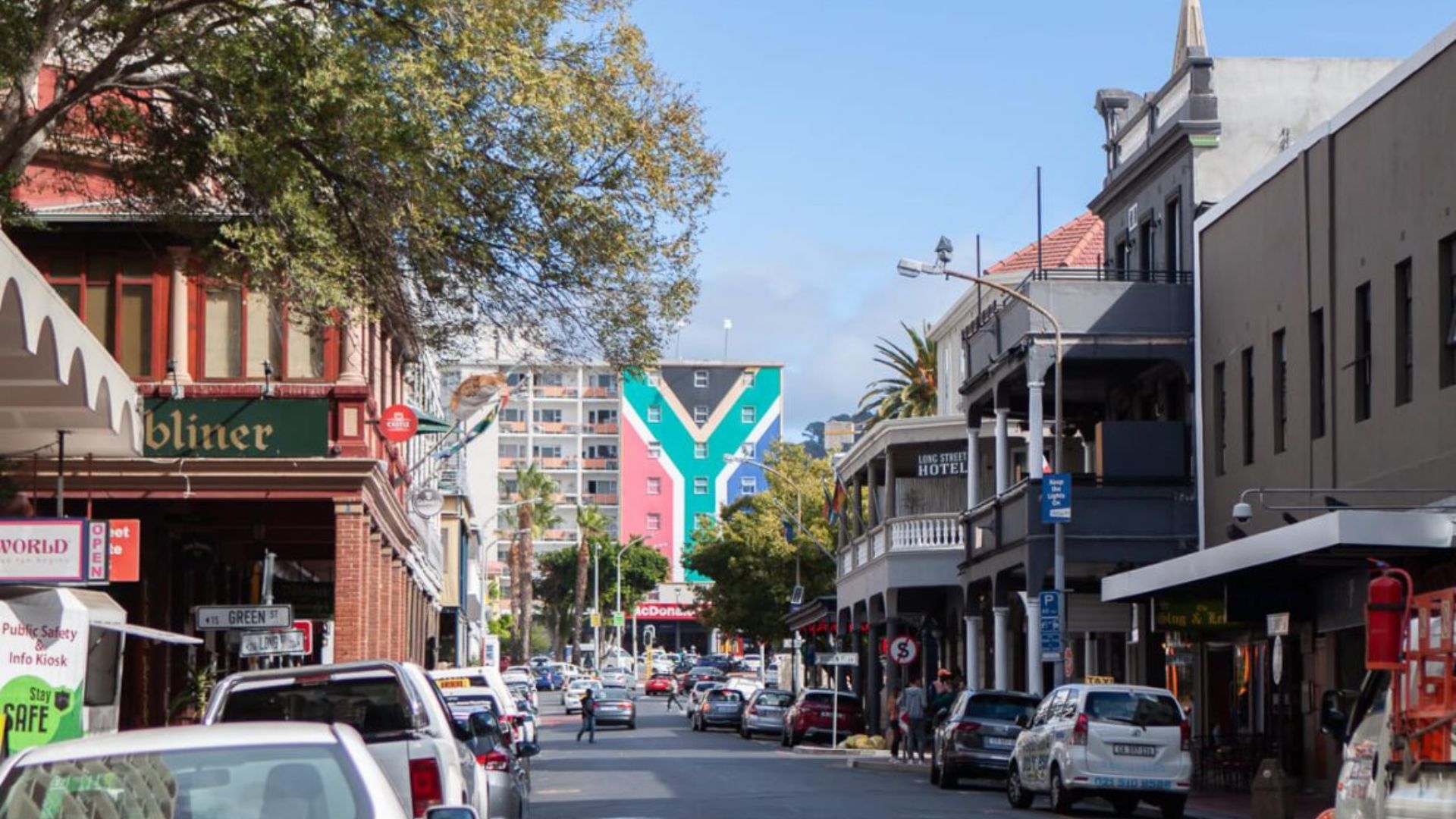 A city street lined with parked cars on both sides, showcasing urban life and traffic patterns.