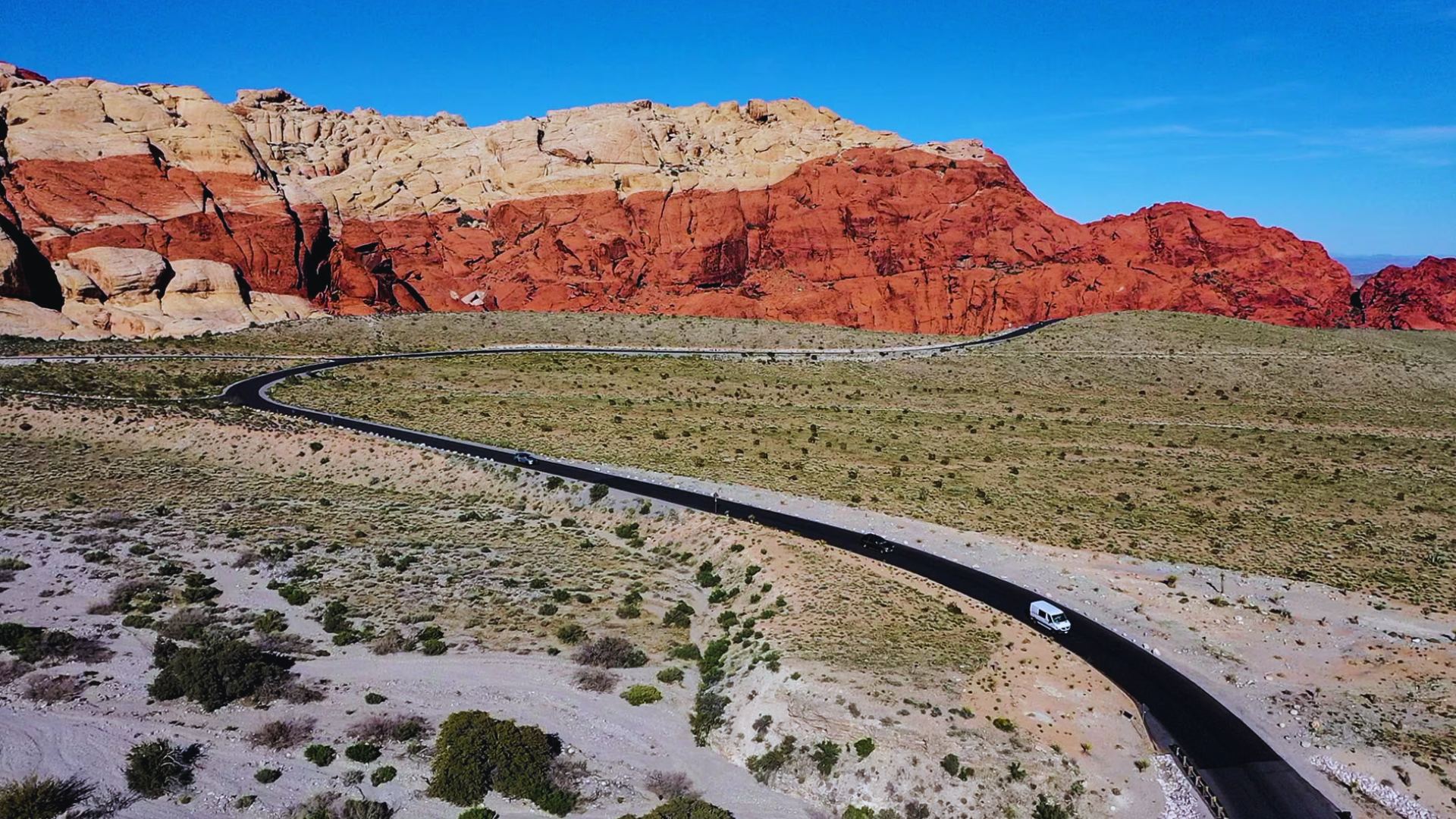 A car drives along a road with a mountain backdrop, showcasing a scenic landscape.