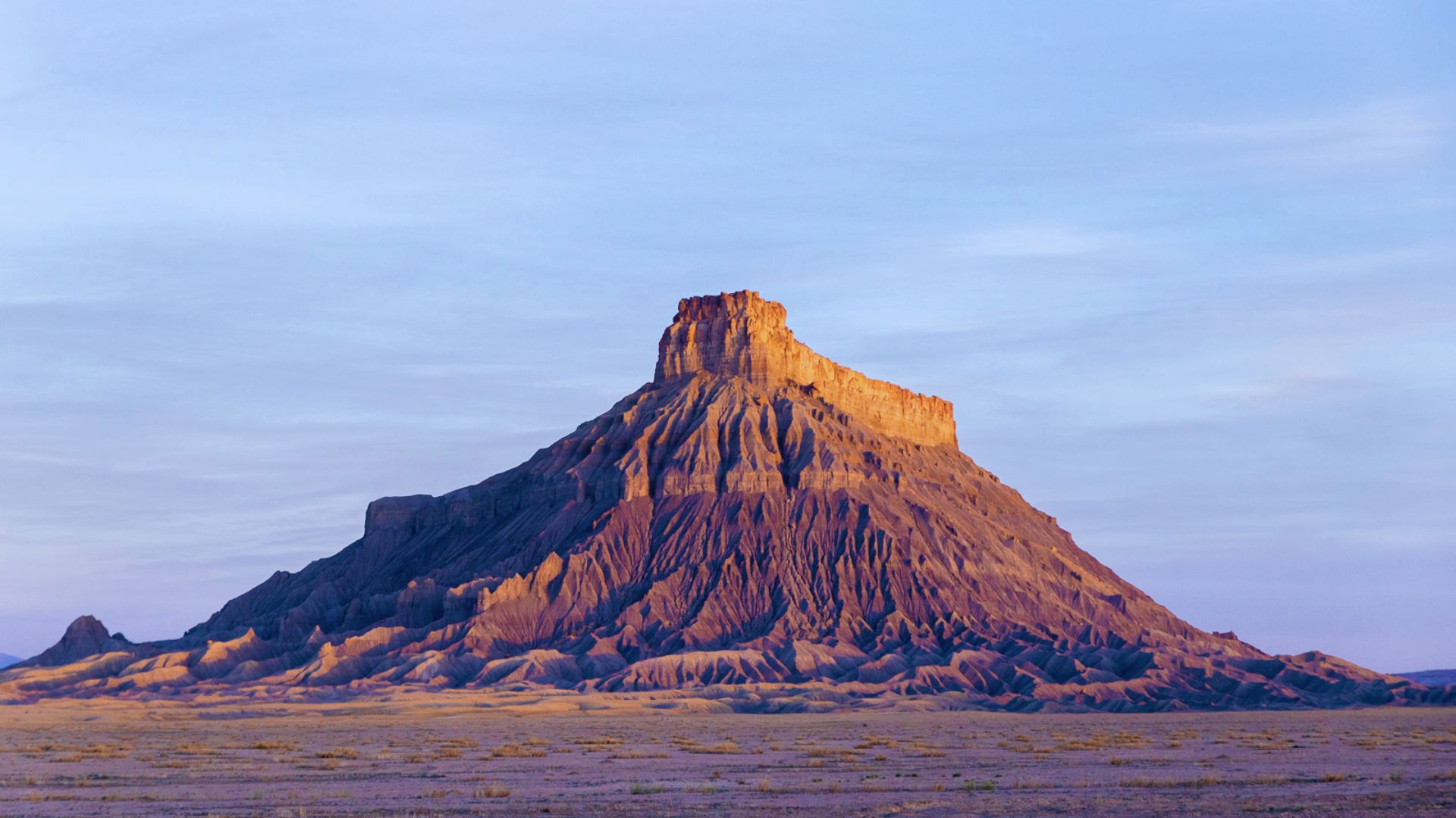 A large mountain rises prominently in a vast desert landscape under a clear blue sky.