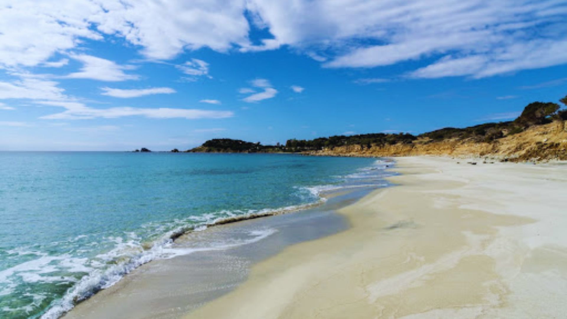 A serene beachscape with turquoise water gently lapping against golden sand under a bright blue sky dotted with scattered clouds, evoking tranquility.