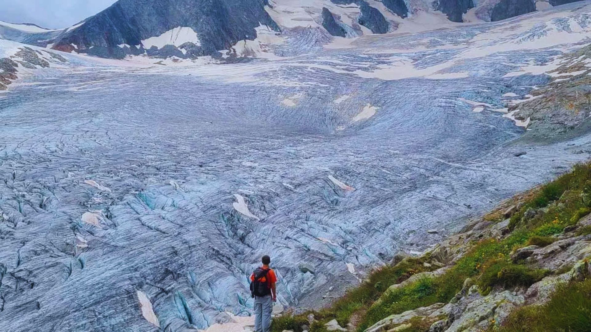 A man hikes up a mountain with a glacier visible in the background, showcasing a stunning natural landscape