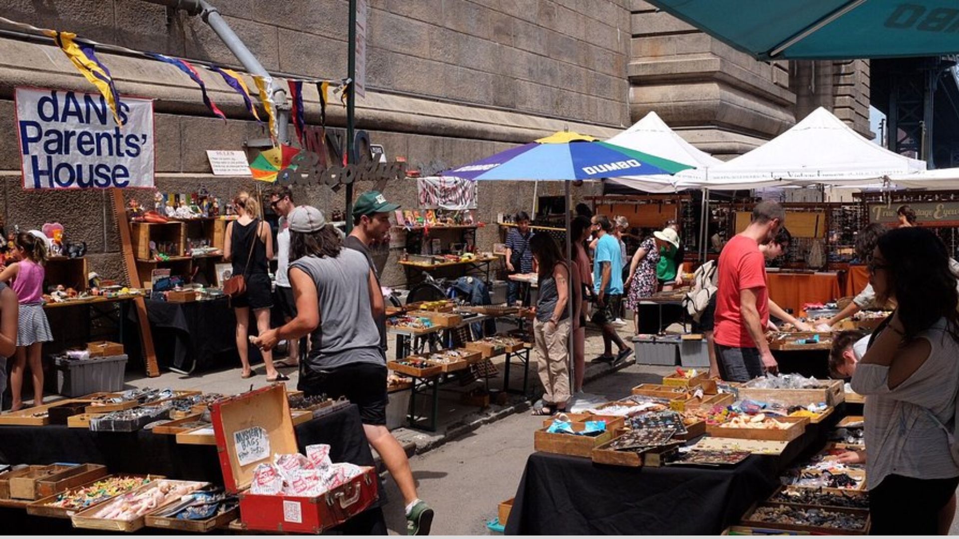 A bustling street market filled with shoppers browsing various stalls and vendors selling fresh produce and goods.