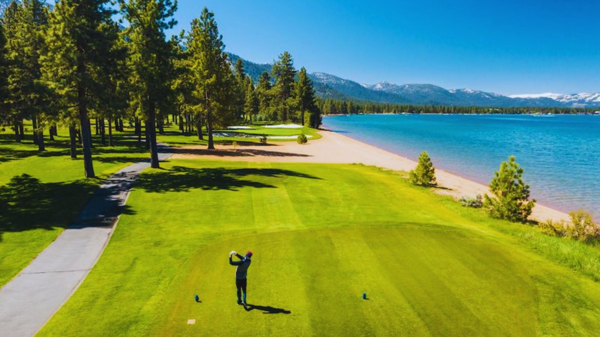 A man swings a golf club on a green, with a serene lake visible in the background.