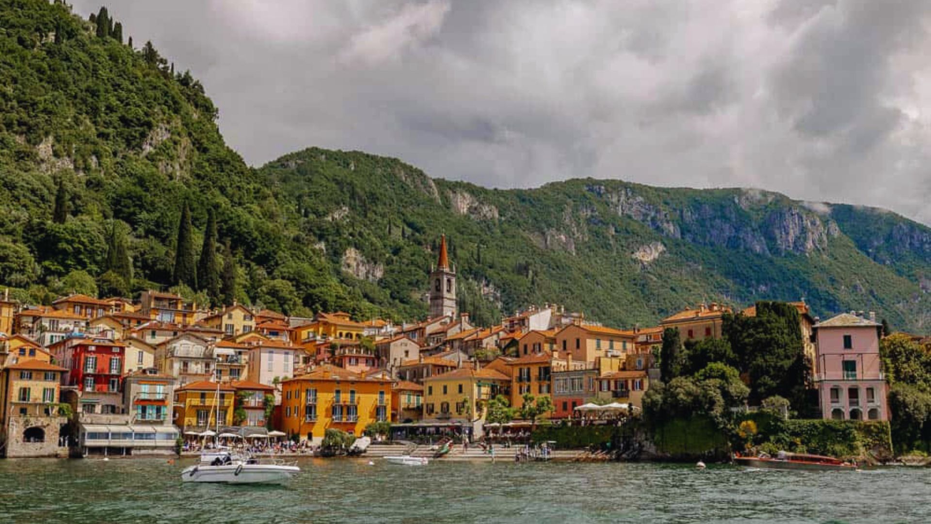 A scenic town by the lake featuring several boats floating on the water under a clear blue sky.