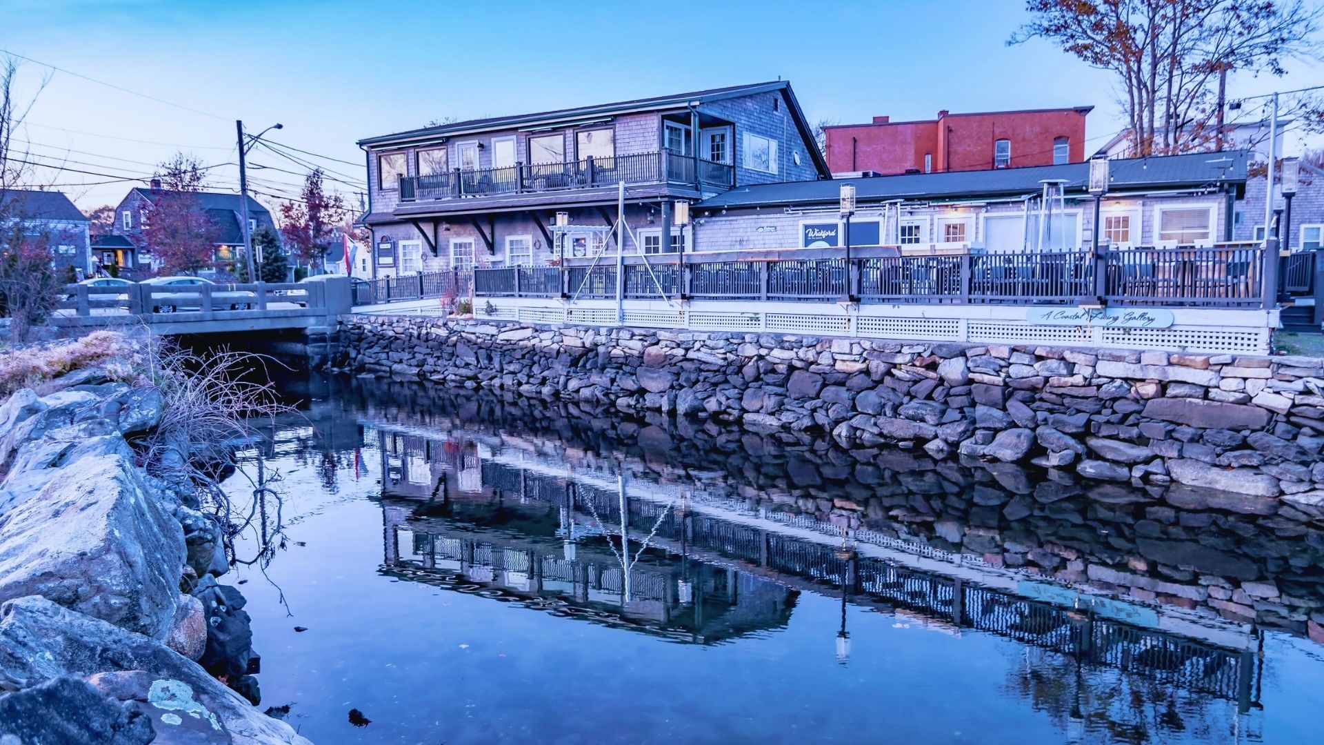 A house is reflected in the water beside a bridge, creating a serene and picturesque landscape.