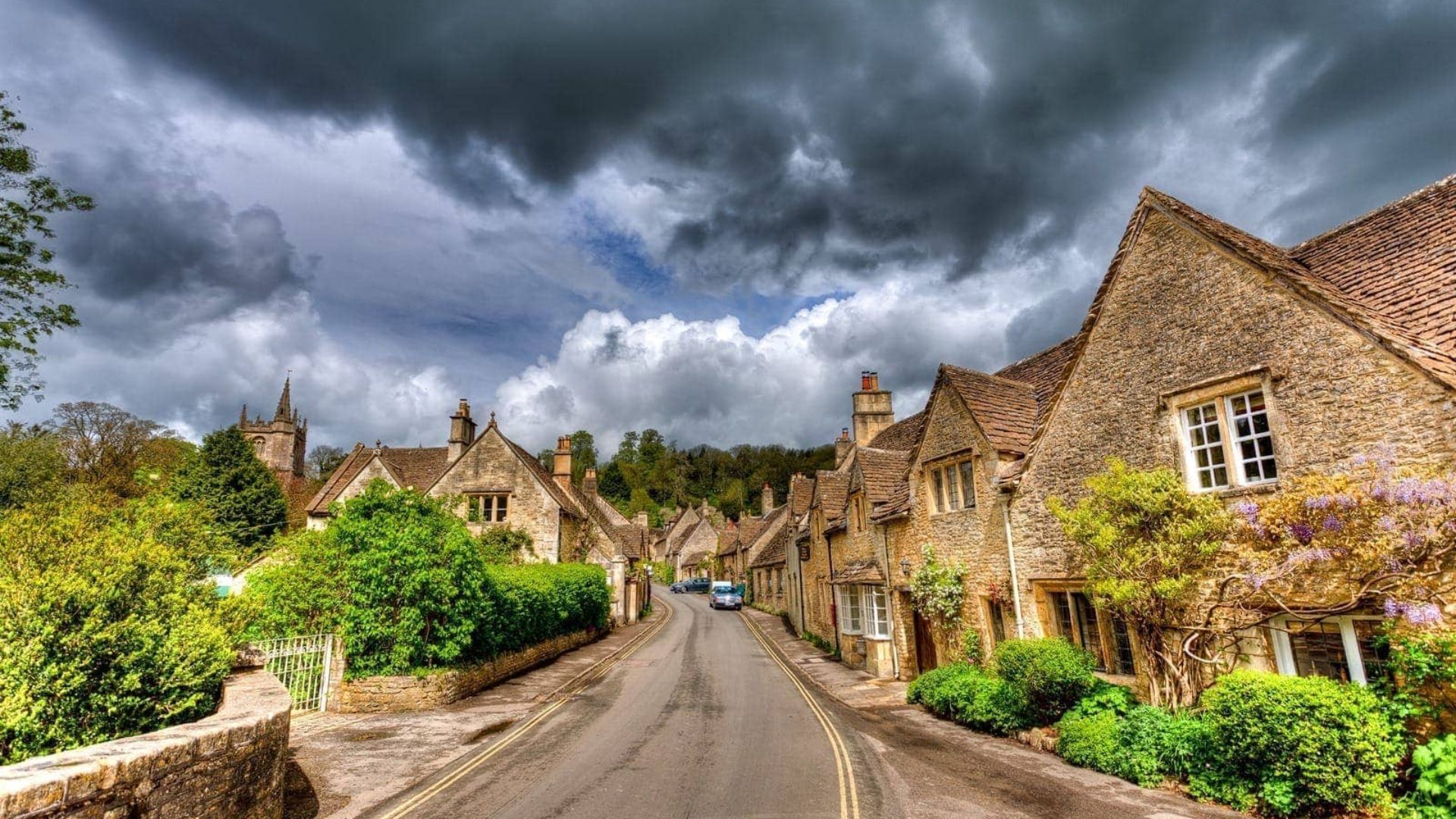 A picturesque street in the Cotswolds, England, lined with charming stone cottages and lush greenery.