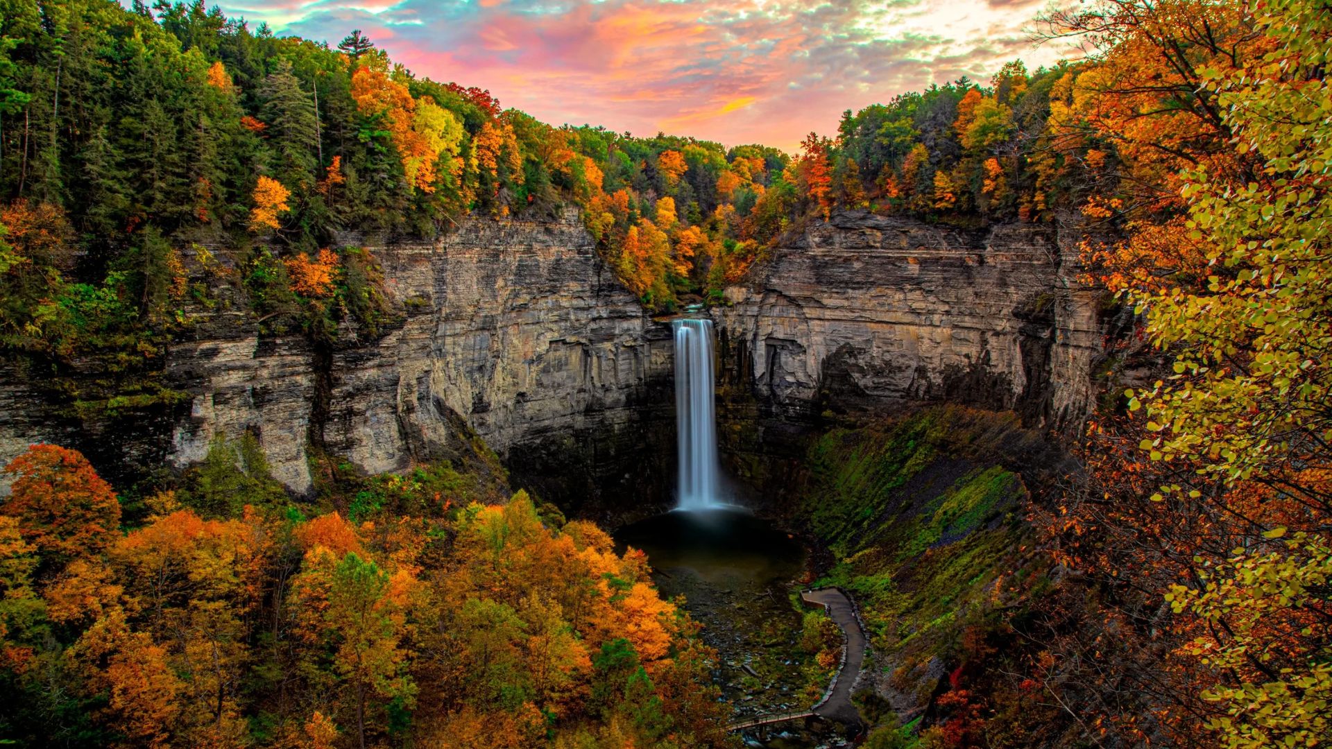 A vibrant waterfall cascades down, surrounded by trees displaying a spectrum of autumn colors.