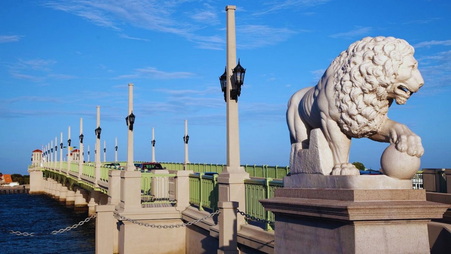 A lion statue stands majestically on a bridge overlooking a serene body of water.