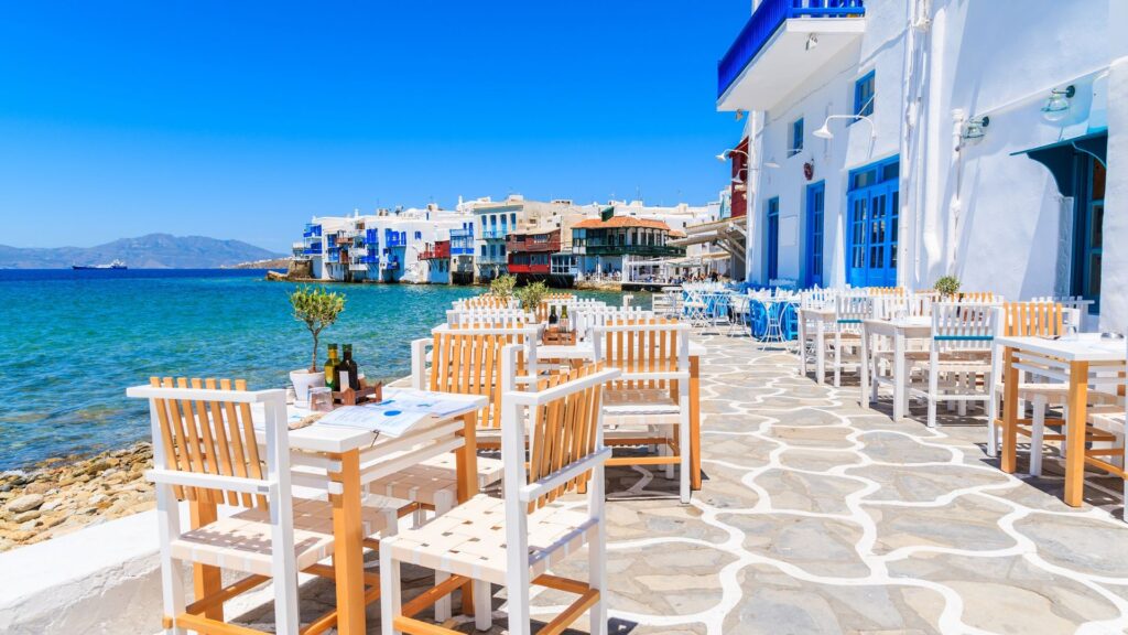 A beachside restaurant featuring white chairs and tables, with a scenic view of the ocean in the background.
