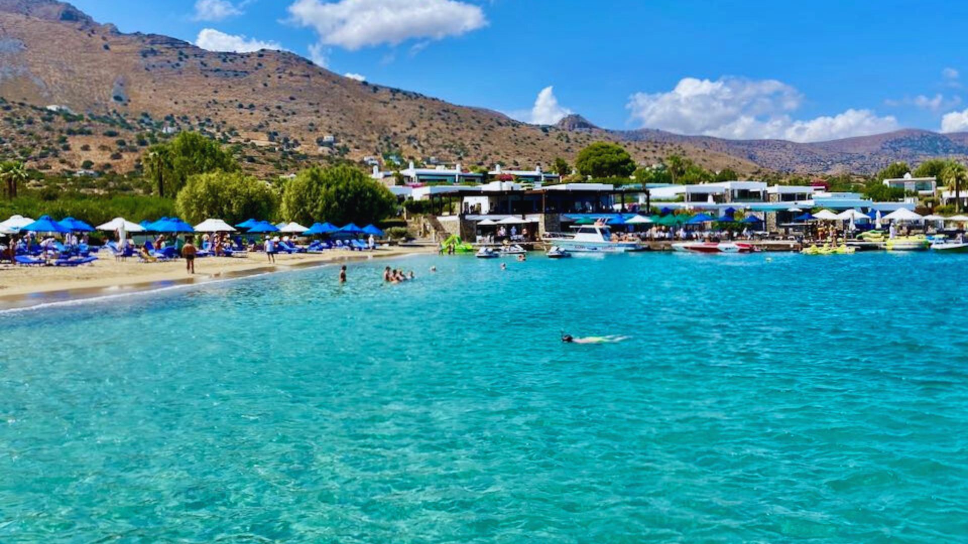 A scenic view of Kalymnos beach in Greece, featuring golden sand, clear blue waters, and surrounding rocky cliffs.