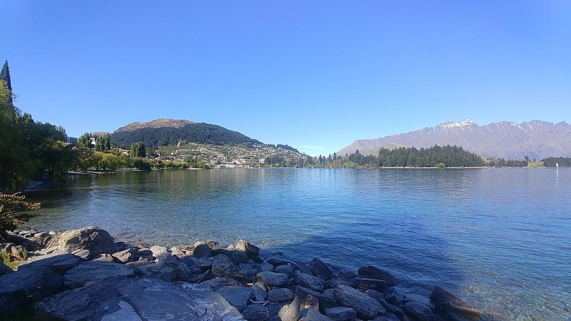A serene lake surrounded by rocks and trees in the foreground, reflecting the natural beauty of the landscape.